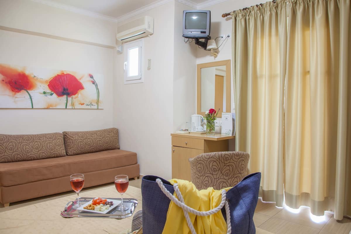 A living room with a sofa, a dining table with a tray of food and drinks, a television, a mirror, and curtains.