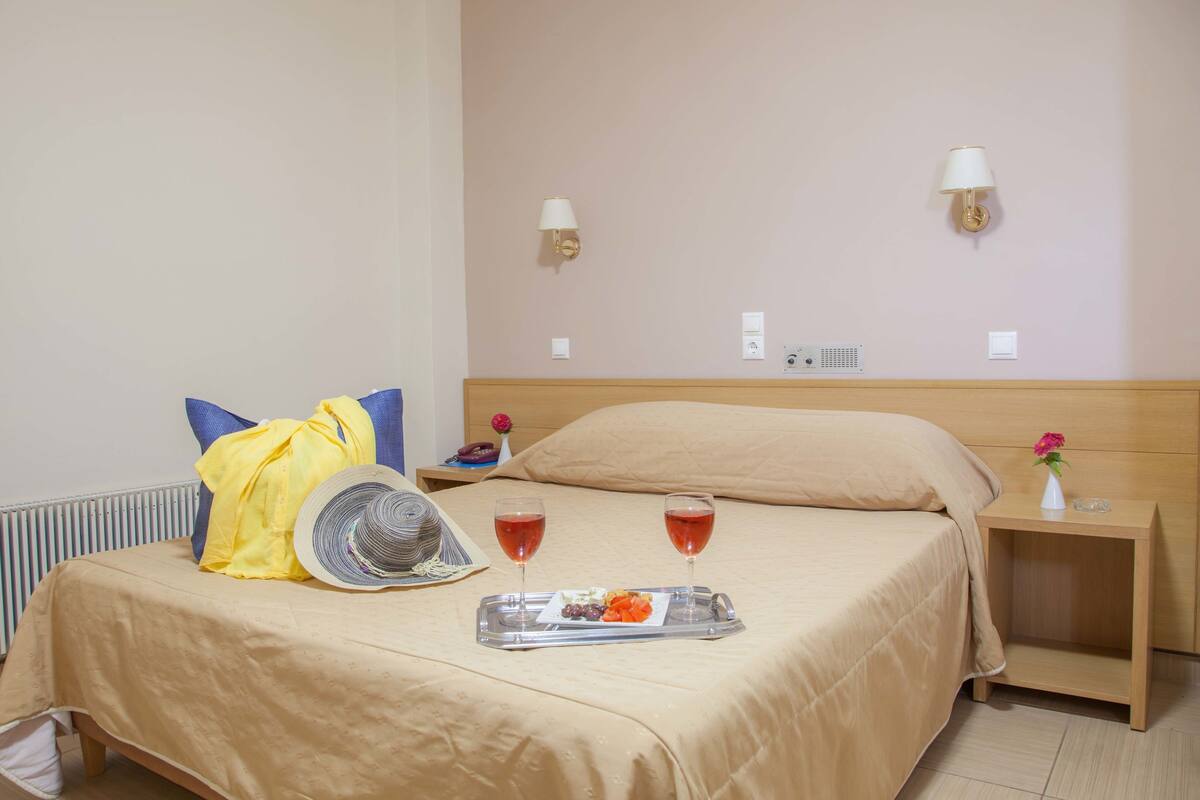 A hotel room with a bed, bedside tables, a tray with snacks and drinks, and a lamp on the wall.