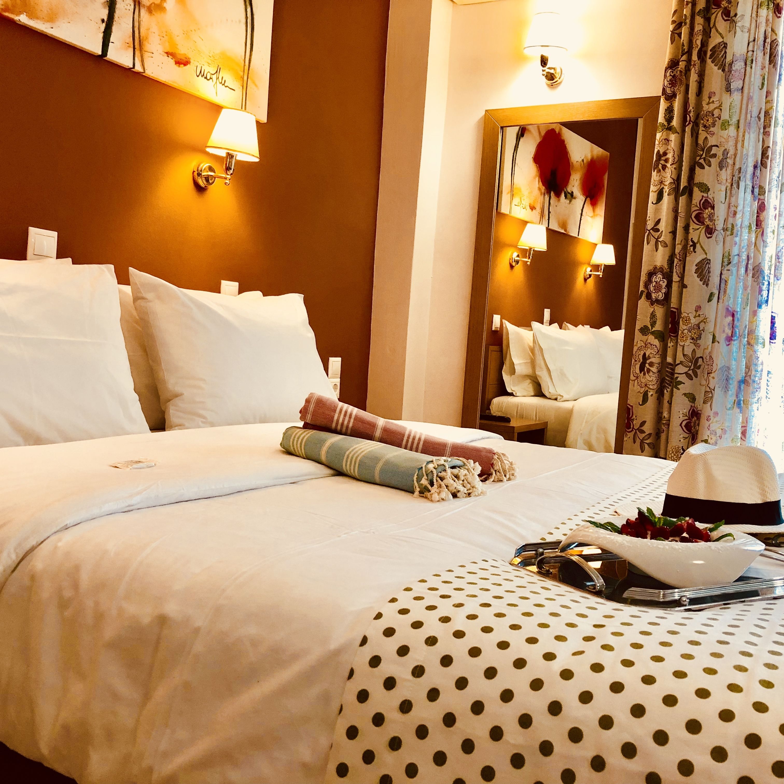 Una camera d'albergo con un letto rifatto, uno specchio e una finestra con tende a fiori.