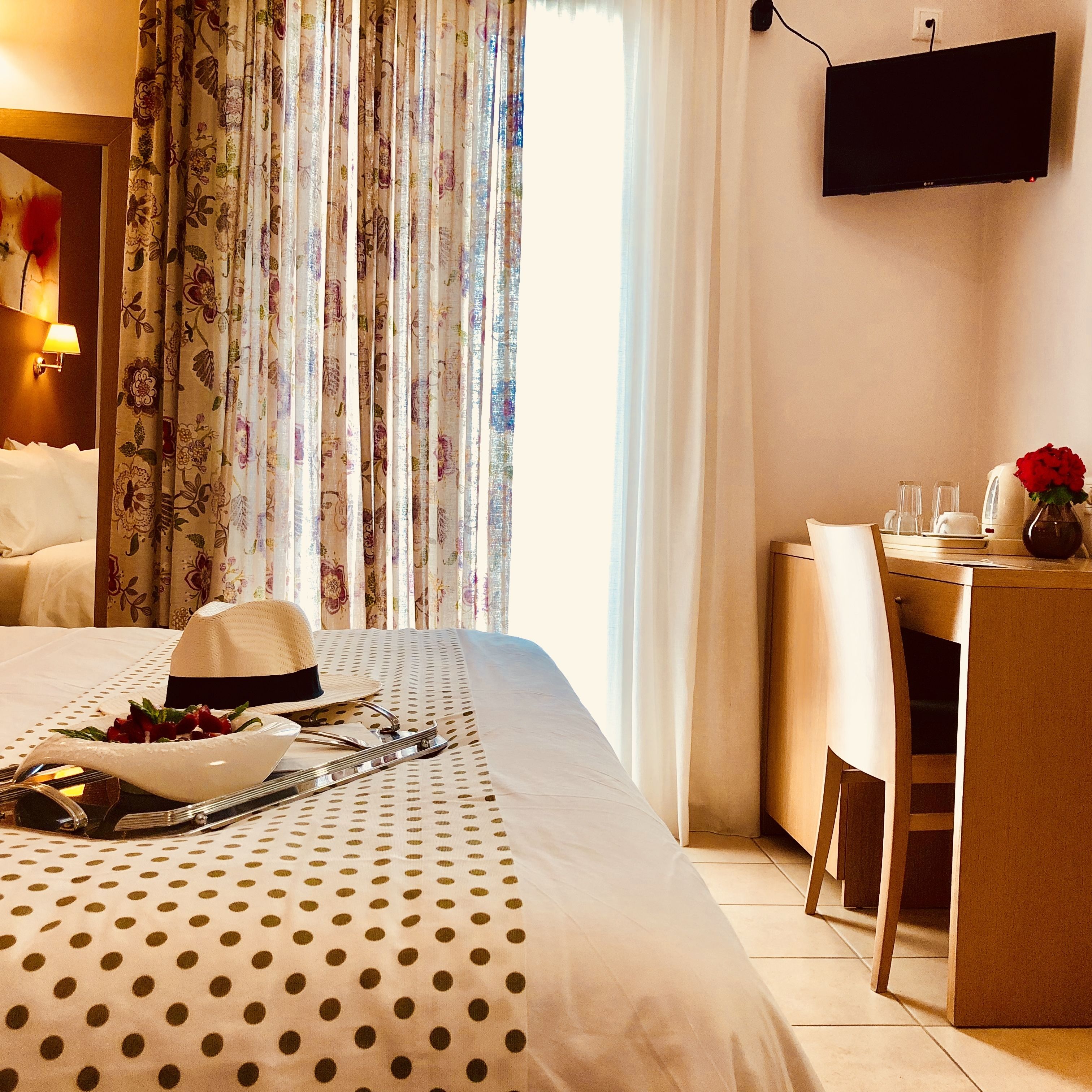 Una camera d'albergo con un letto, una scrivania, una televisione e una finestra con tende.