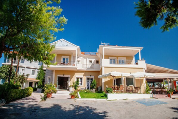 A two-story hotel with a balcony, outdoor seating area, and a well-maintained garden. - George (Lefkada)