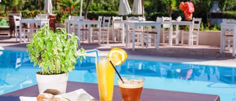 A poolside table with croissants, a drink with a lemon slice, and a potted plant.