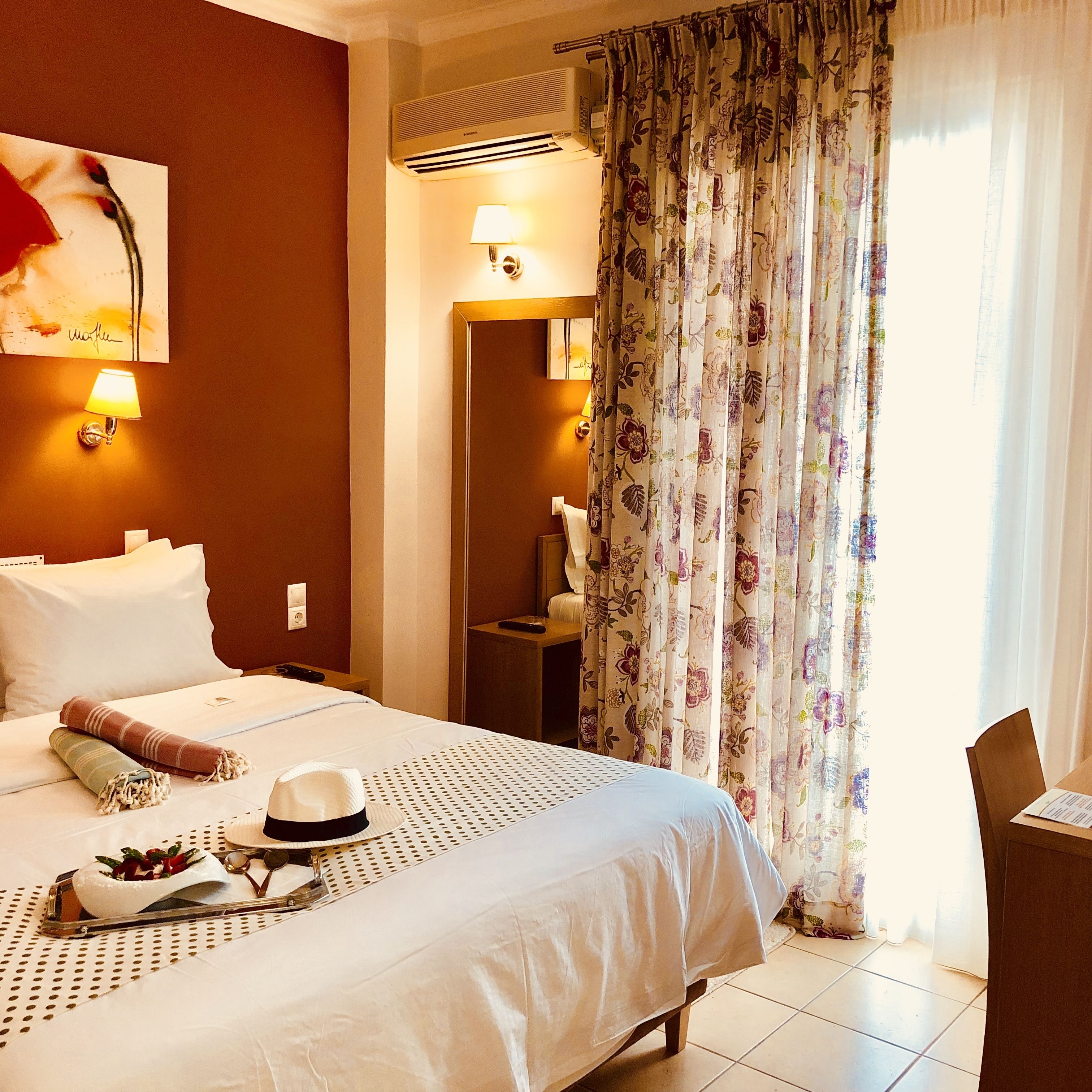 A hotel room with a bed, a desk, a chair, a lamp, and a window with curtains.