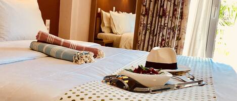 A hotel room with a bed, a polka dot table runner, a hat, and a tray with cutlery and a bowl of fruit.