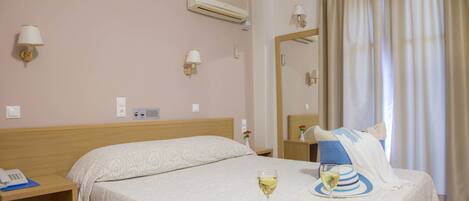 Habitación de hotel con cama, mesitas de noche, aire acondicionado, espejo y ventana con cortinas.