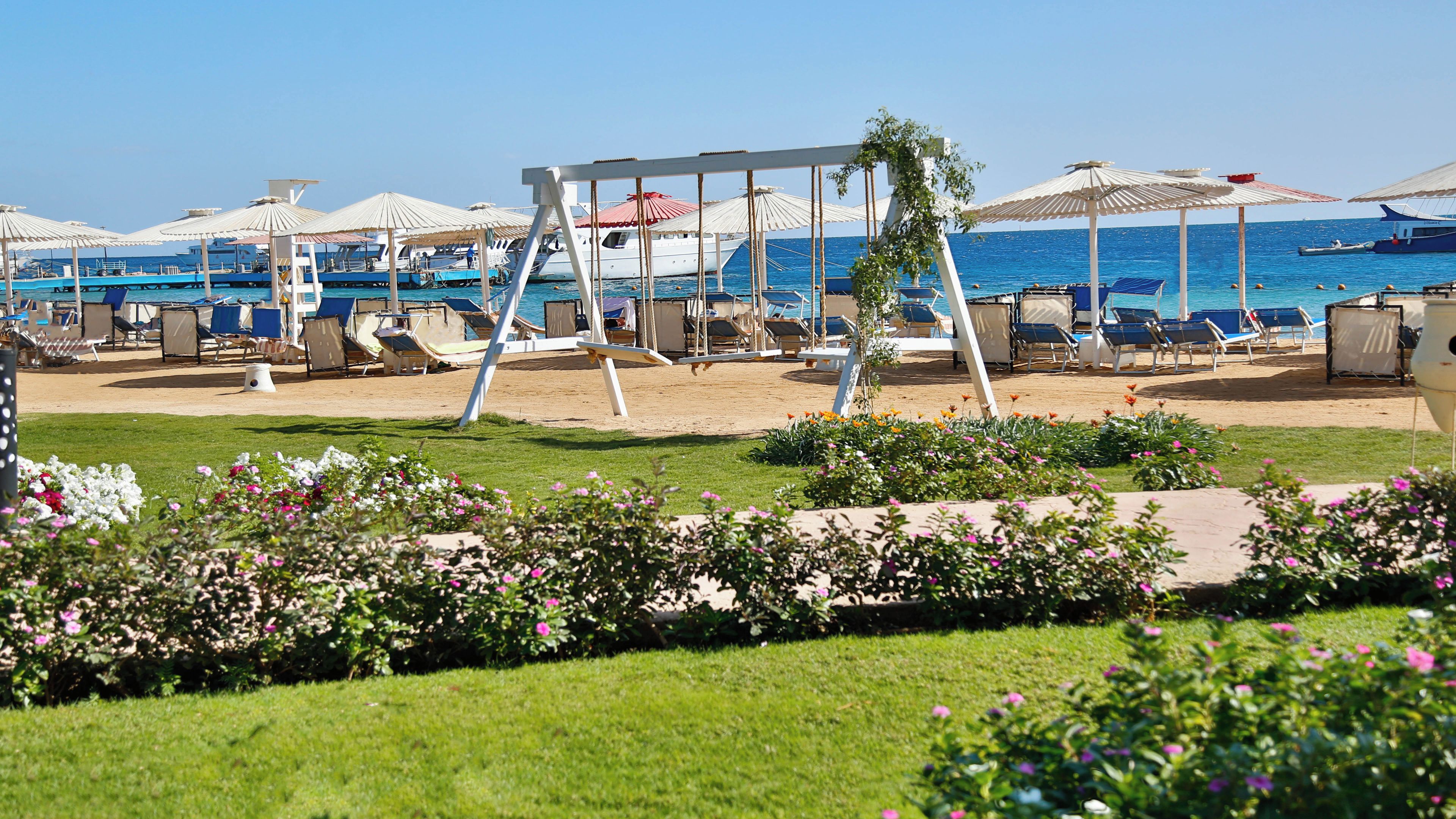 A beachside resort with sun loungers, umbrellas, and boats in the background.