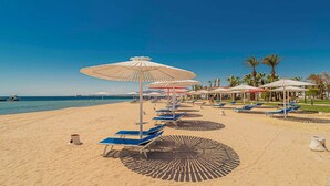 Uma praia com fileiras de espreguiçadeiras e guarda-sóis, céu claro e mar calmo.
