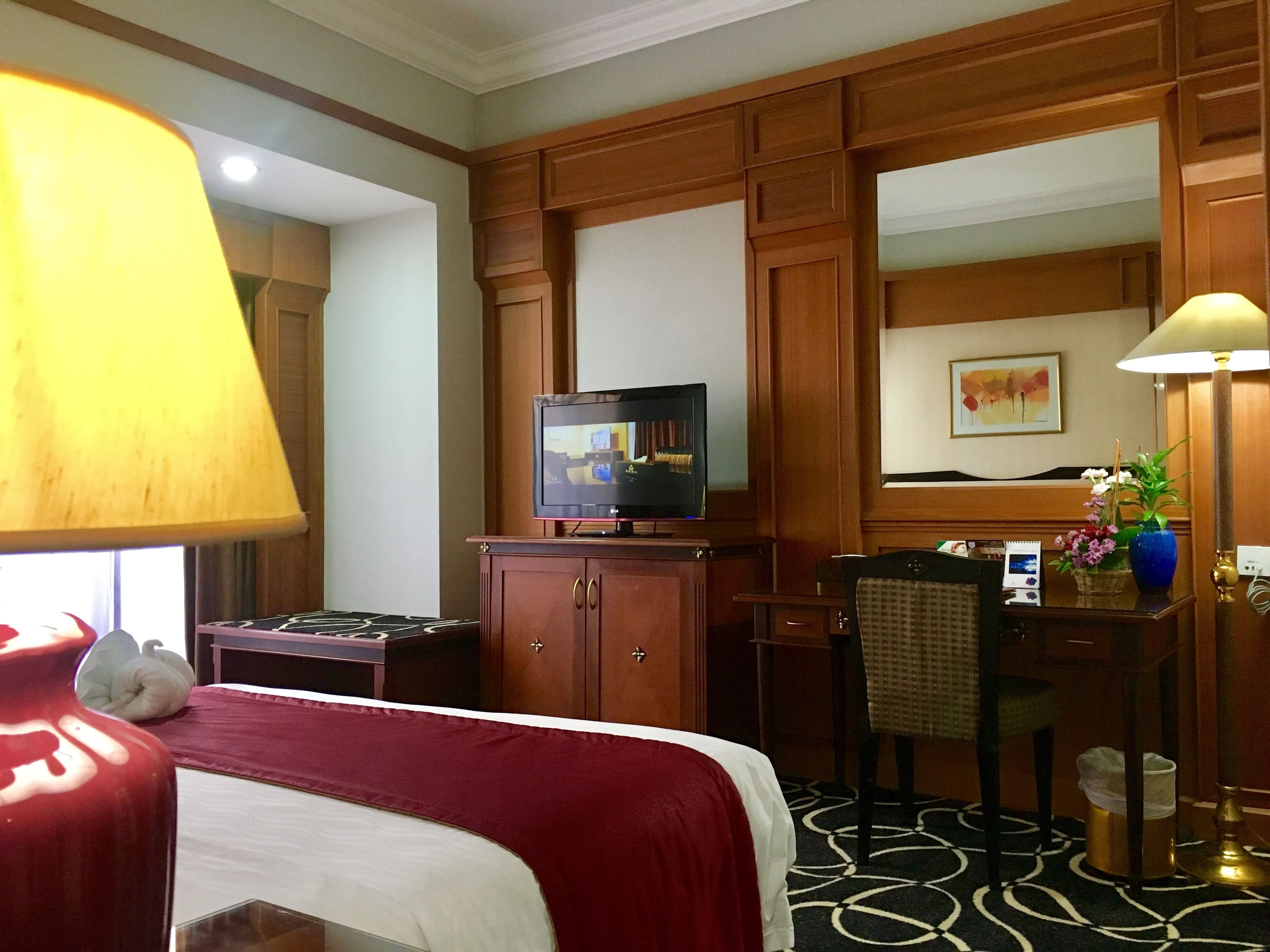 A hotel room with a bed, a desk with a computer, a television, and a lamp.