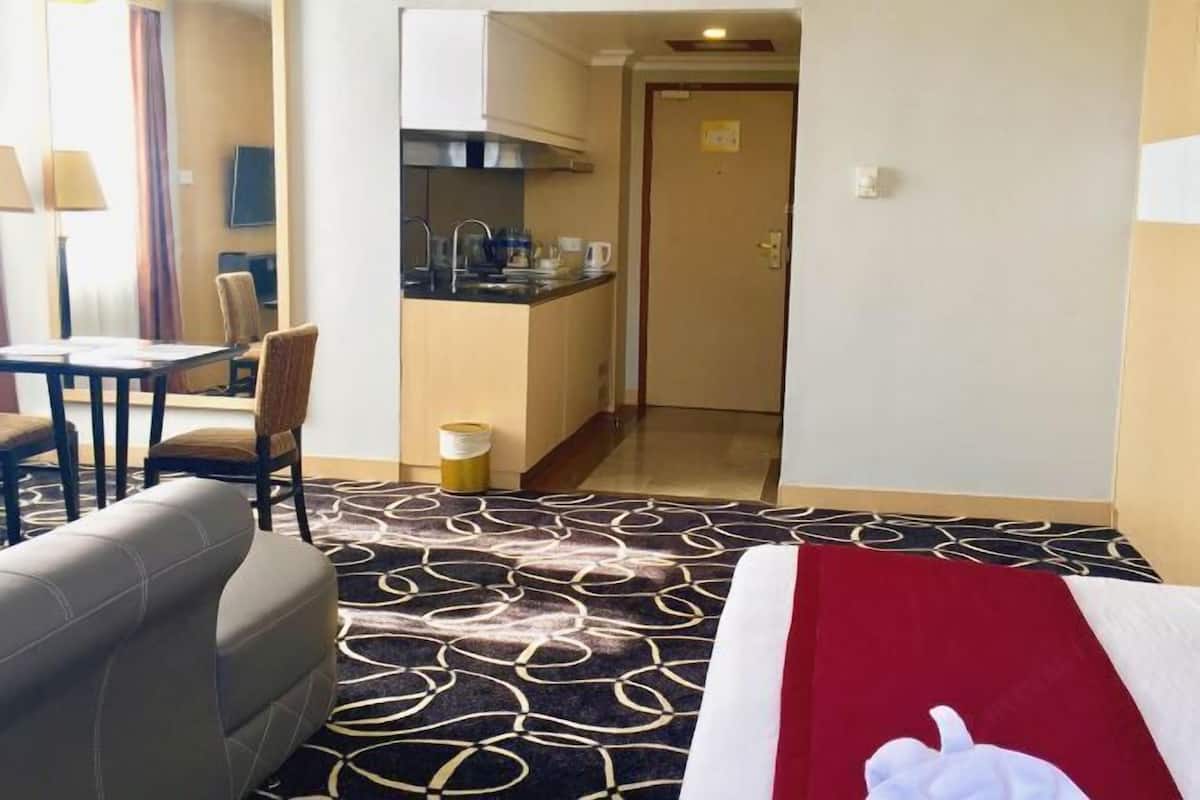 A hotel room with a bed, a sofa, a dining table with chairs, a kitchenette, and a door leading to another room.