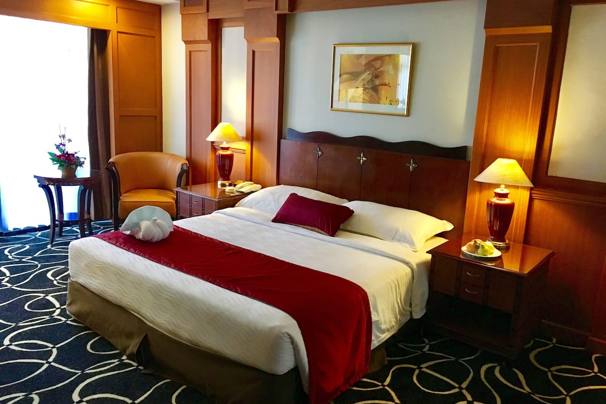 A hotel room with a bed, two bedside tables, a chair, a lamp, and a painting on the wall.