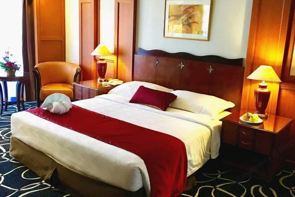 A hotel room with a bed, a chair, a nightstand, a lamp, and a painting on the wall.