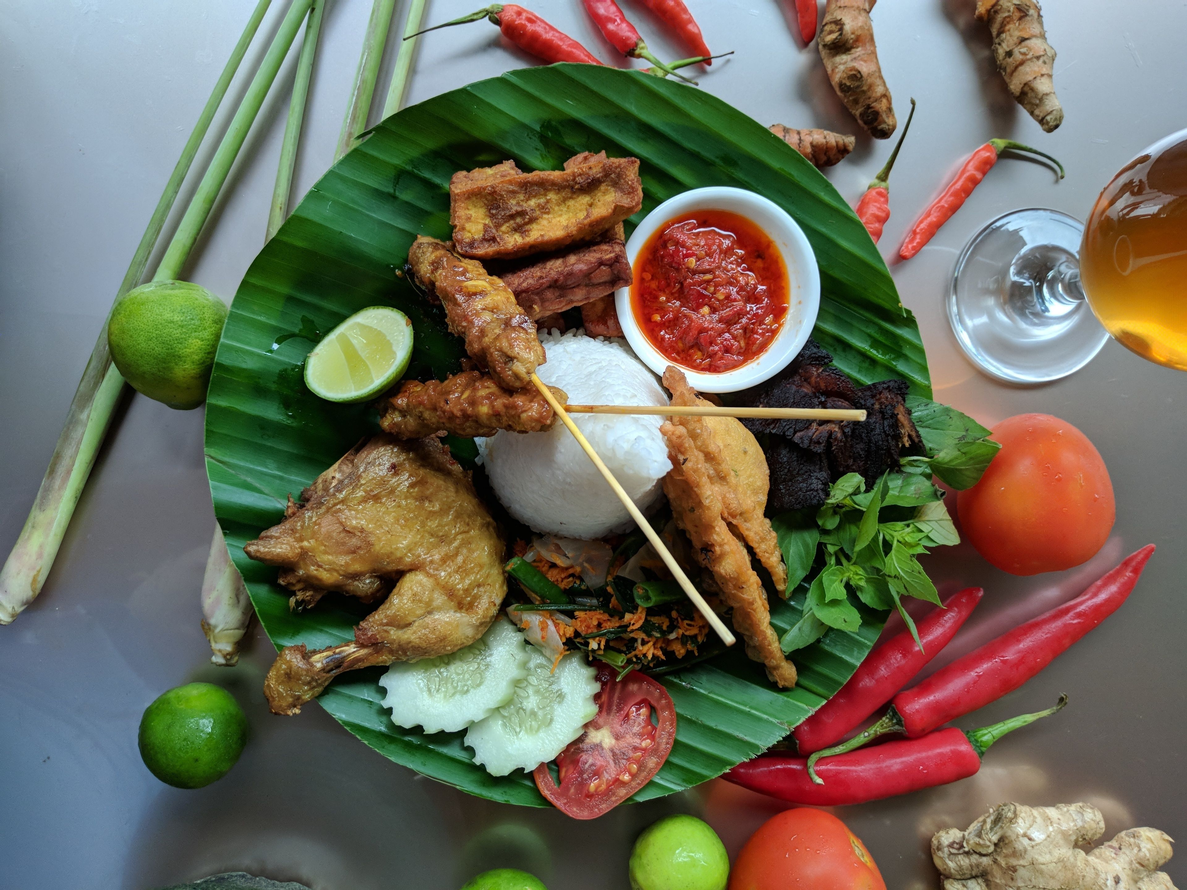 A plate of fried chicken, rice, and vegetables on a banana leaf.