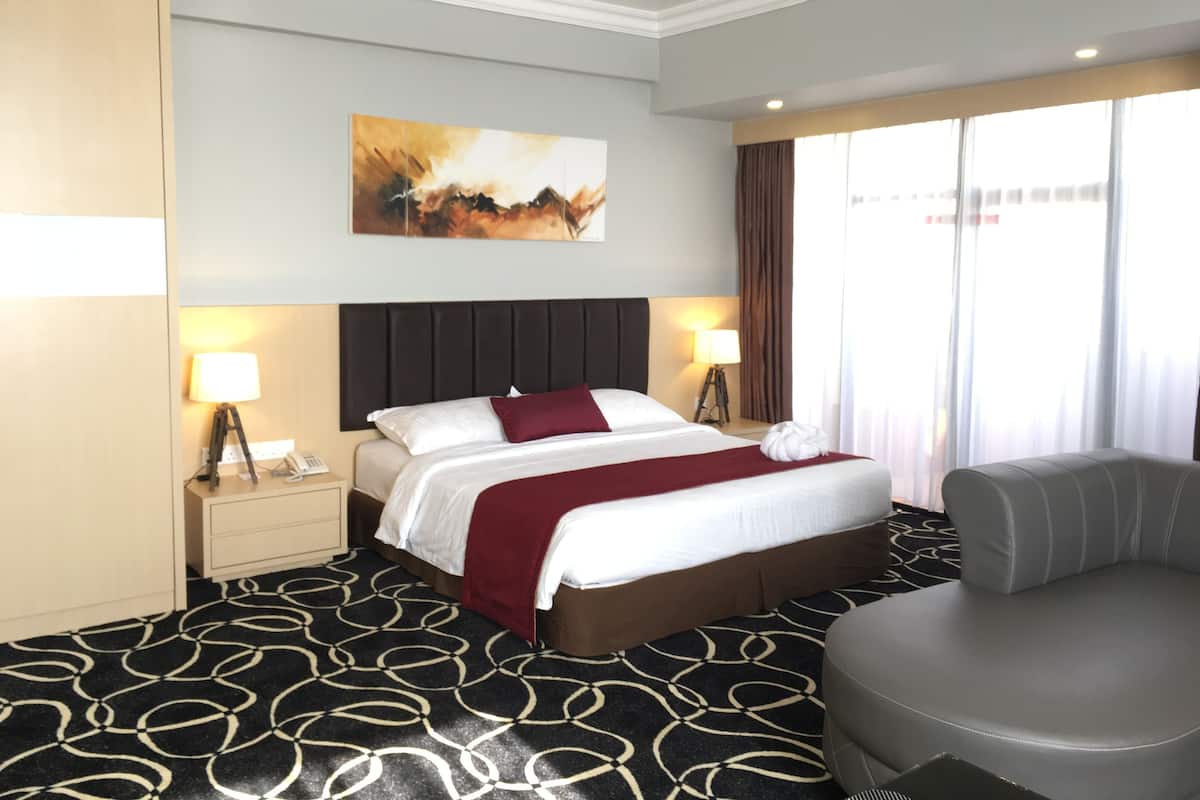 A hotel room with a bed, bedside lamps, a chair, a large window with curtains, and a painting on the wall.