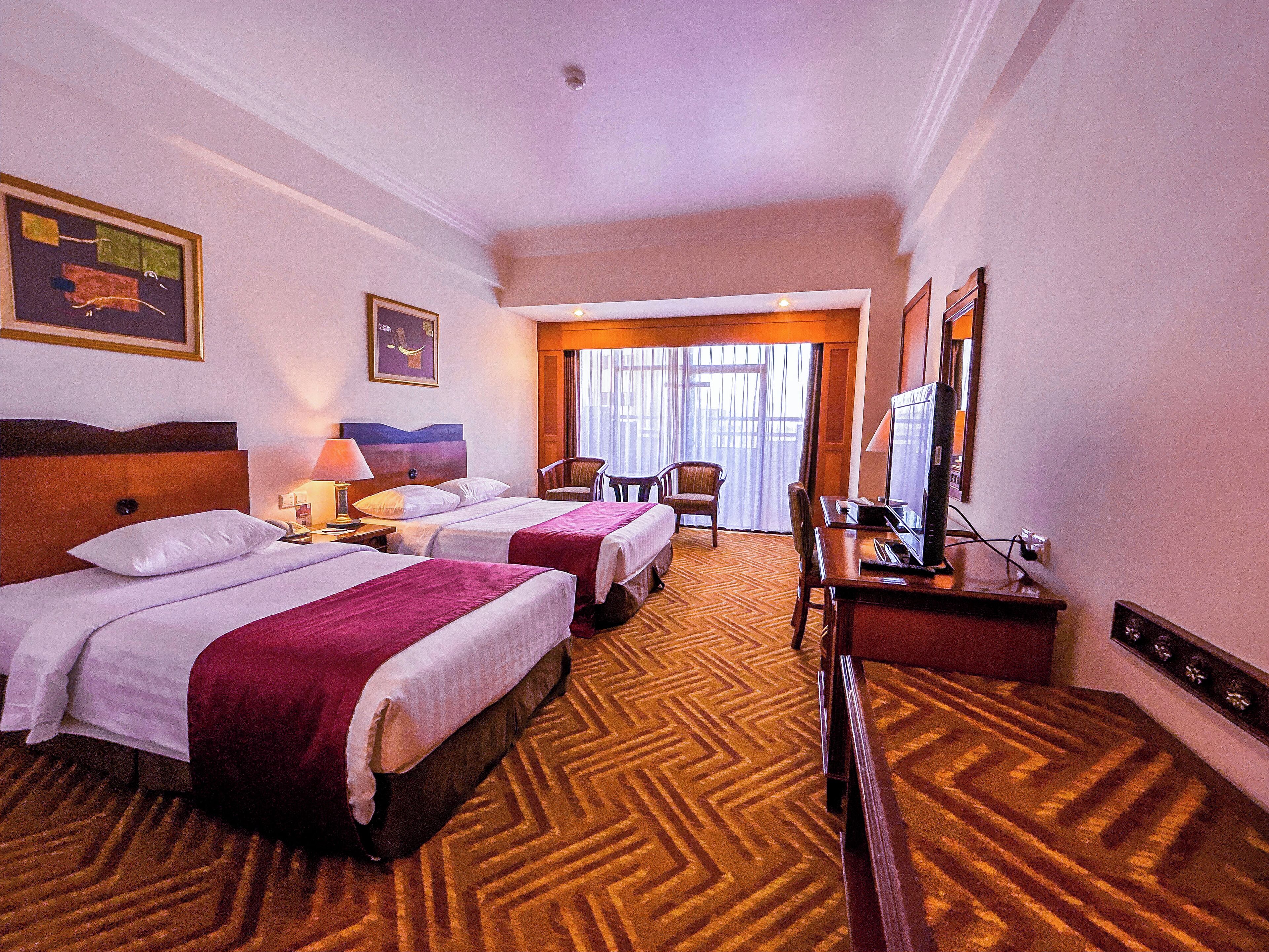 A hotel room with two beds, a desk, a chair, and a television.