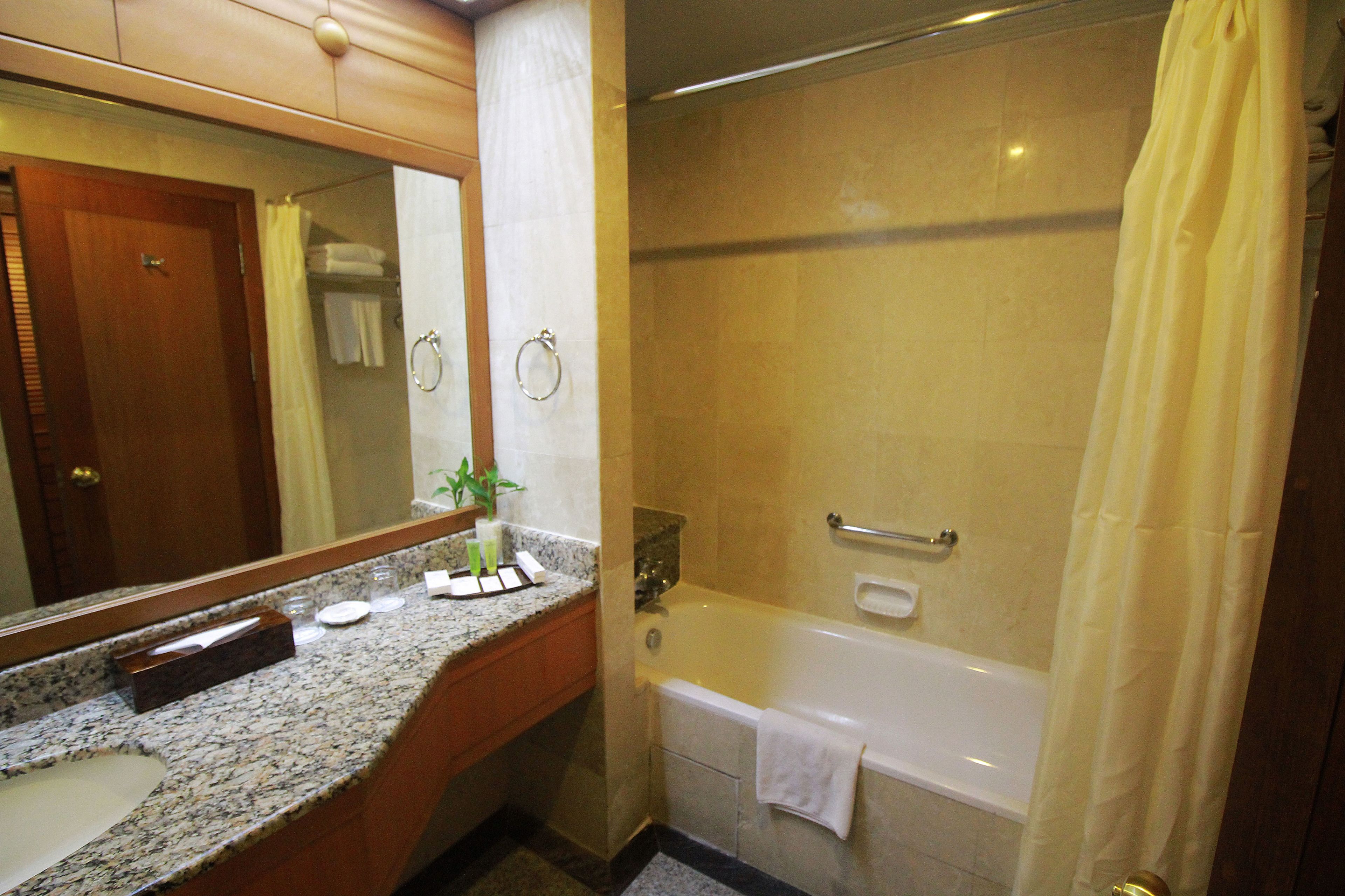 A bathroom with a granite countertop, a sink, a mirror, a bathtub, and a shower curtain.