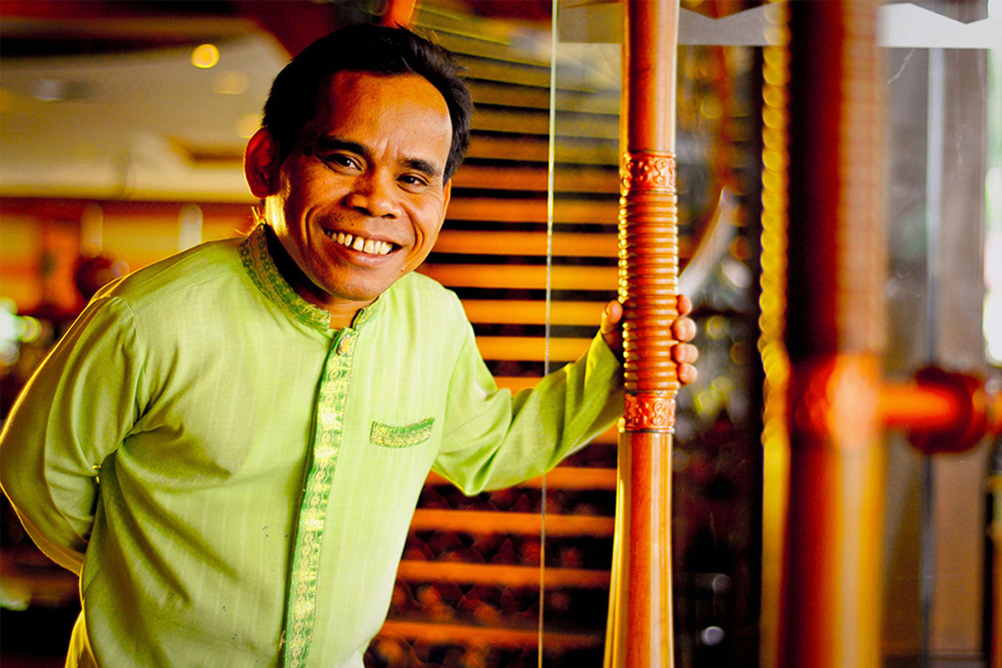 Una persona con camisa verde apoyada en una estructura de madera con un diseño decorativo.