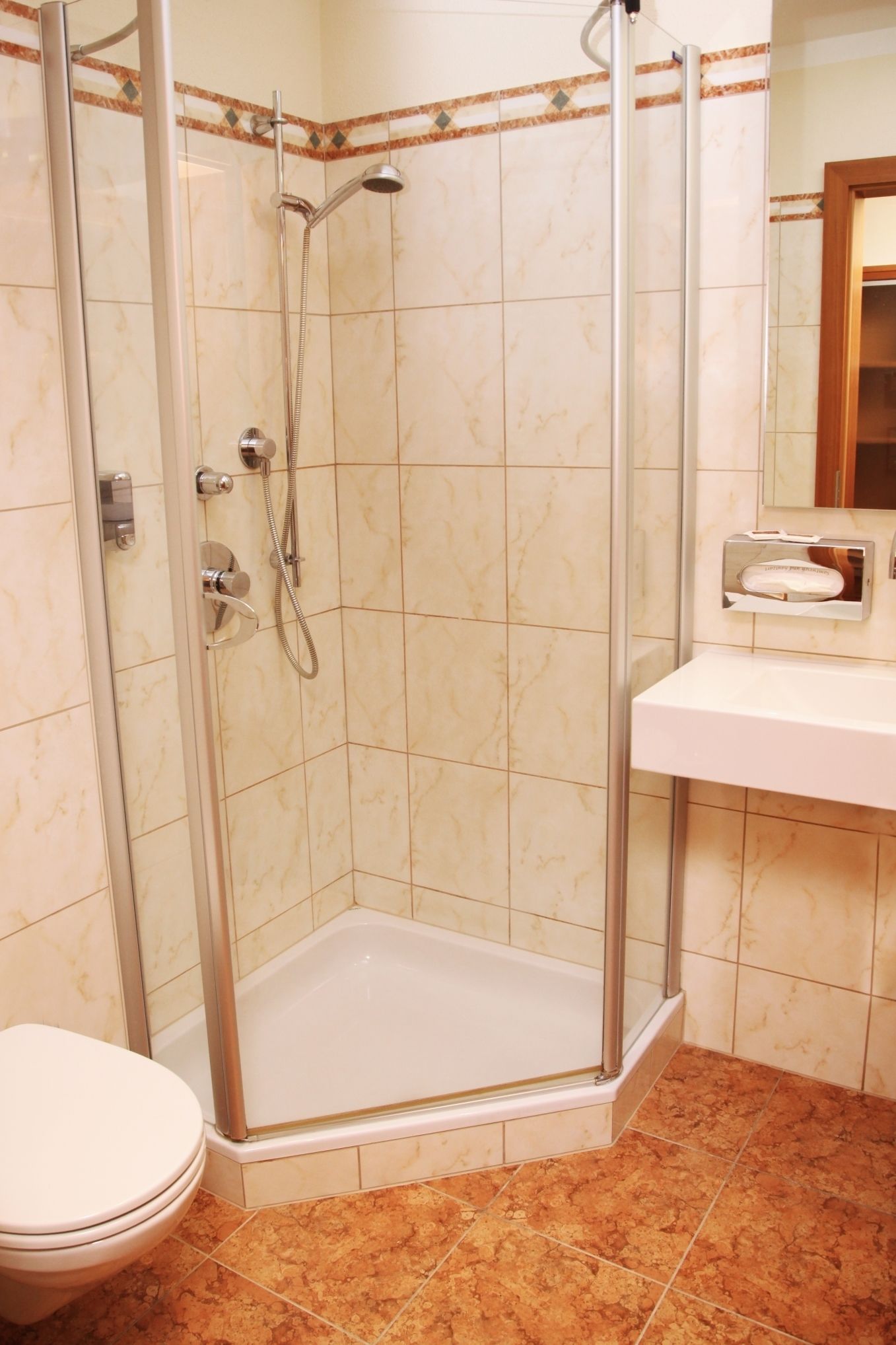 A shower with a glass door, a white toilet, and a bathroom sink with a mirror.