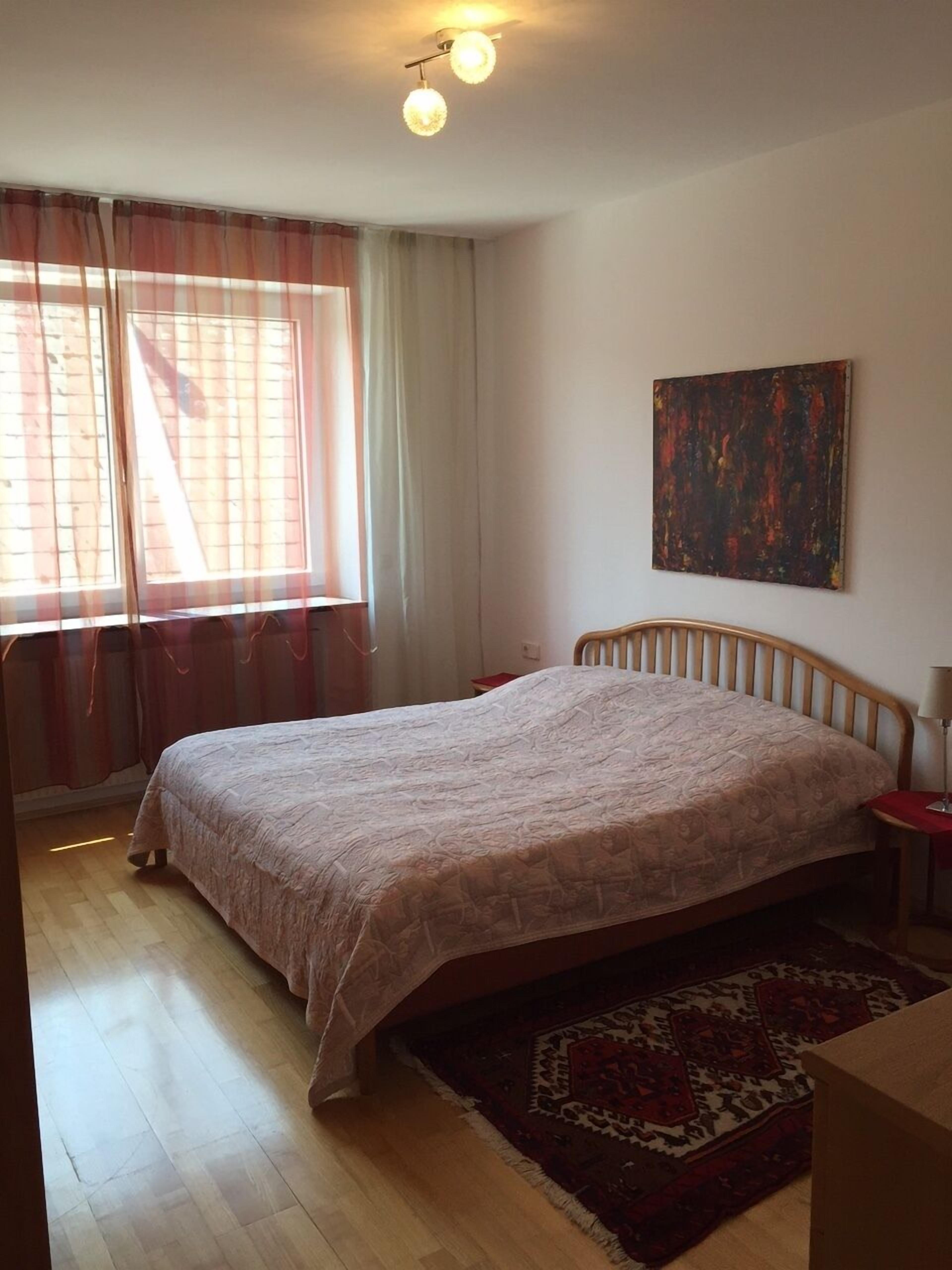 Una camera da letto con un letto, una finestra con tende, un quadro appeso al muro e un tappeto al pavimento.