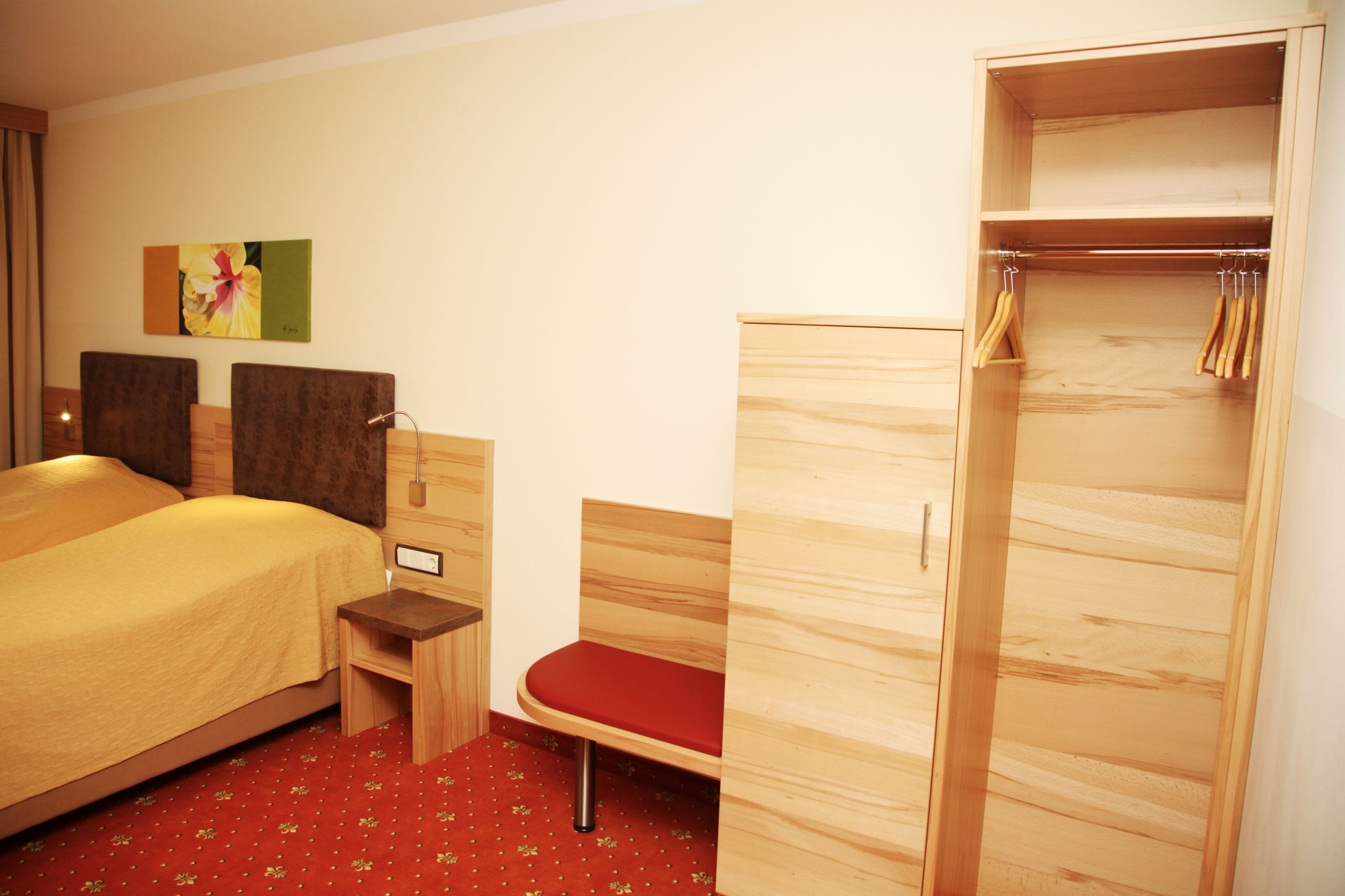 A hotel room with a bed, a wooden wardrobe, a bench, and a small table.