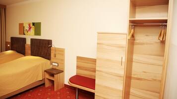 A hotel room with a bed, a wooden wardrobe, a bench, and a small table.