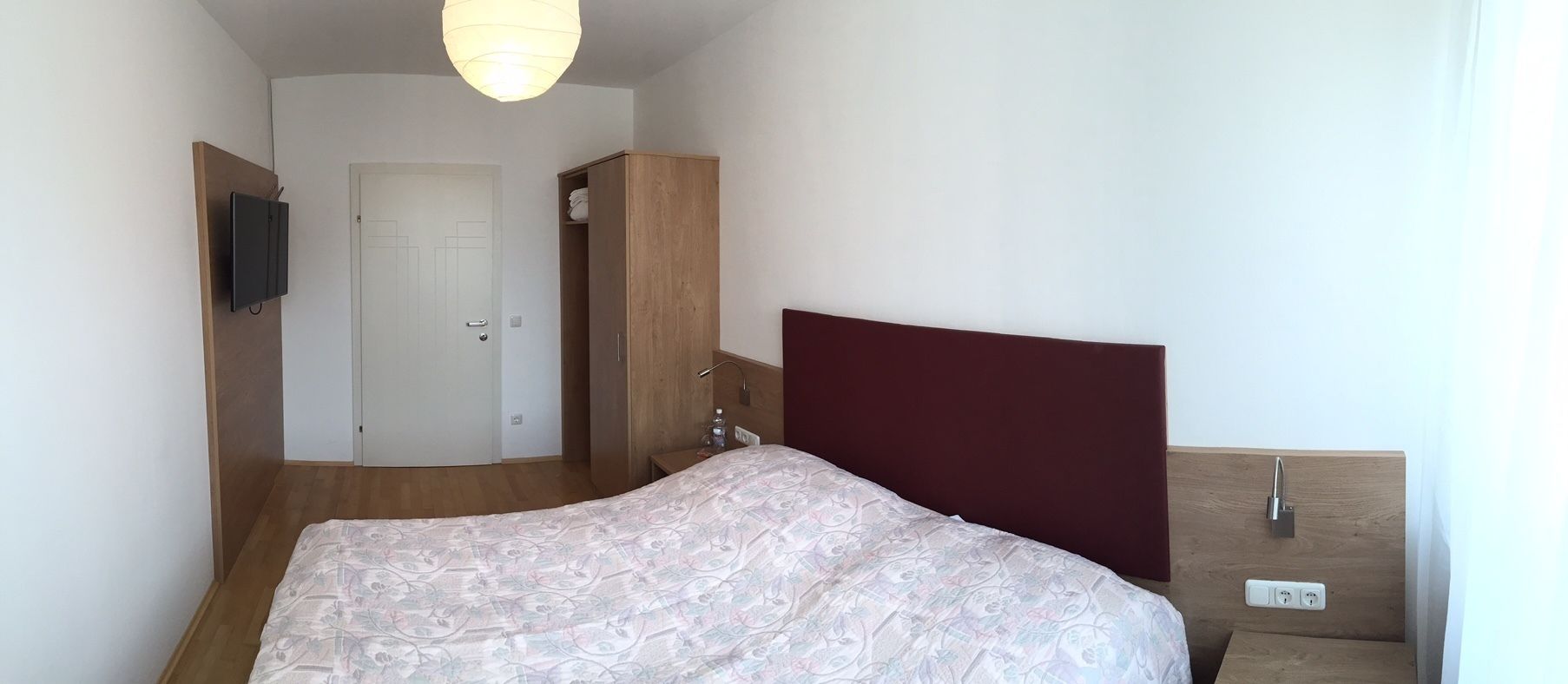 A bedroom with a bed, a wardrobe, a door, and a light fixture.