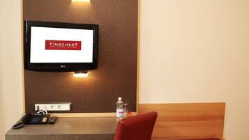 Hotelkamer met een bureau, stoel en een televisie waarop 'TINSCHERT' staat.