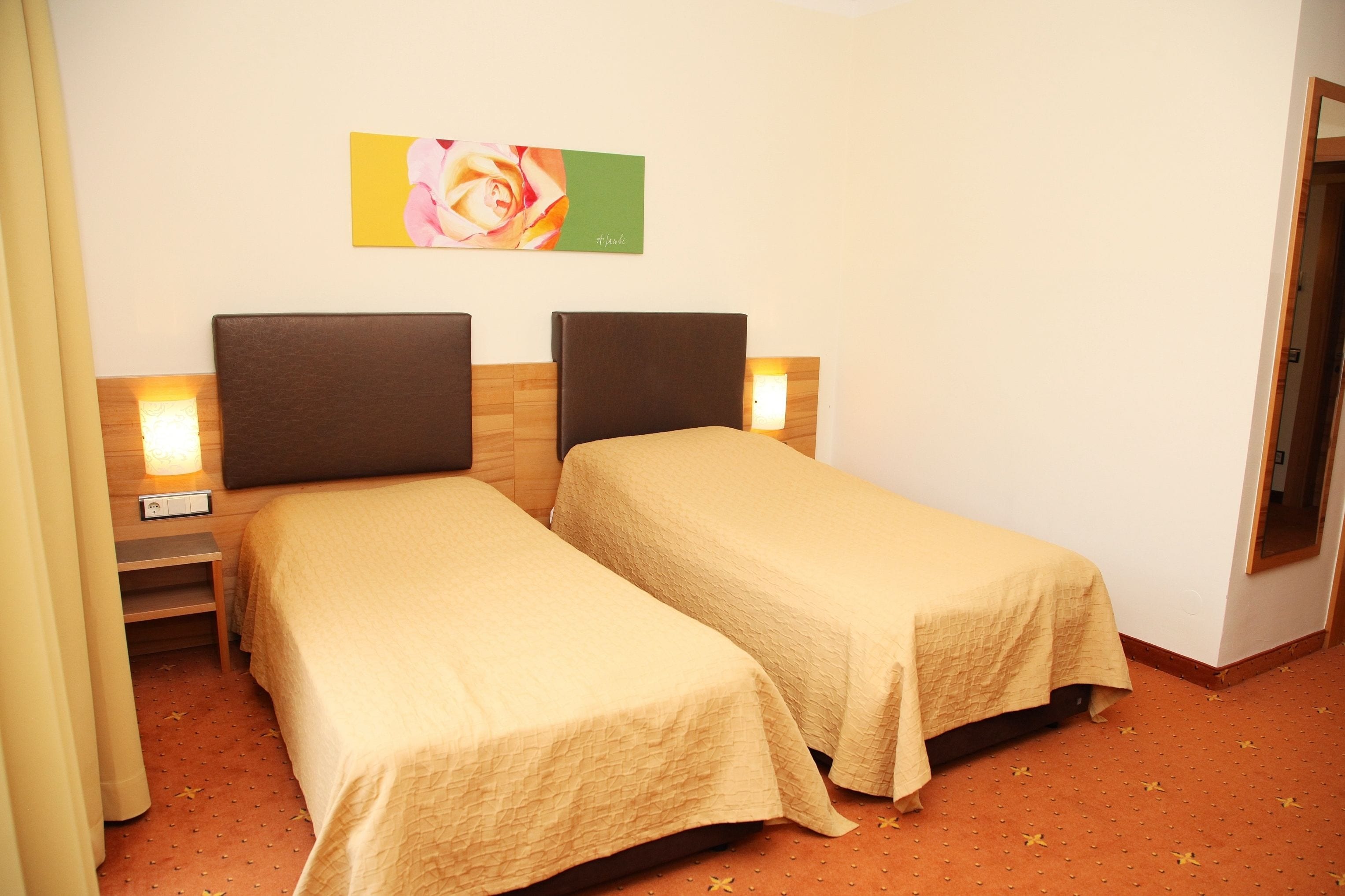 Habitación de hotel con dos camas individuales, una mesita de noche con lámpara, un cuadro en la pared y un cabecero de madera.