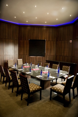 Un salón de conferencias con una gran mesa, sillas y una pantalla para proyector.