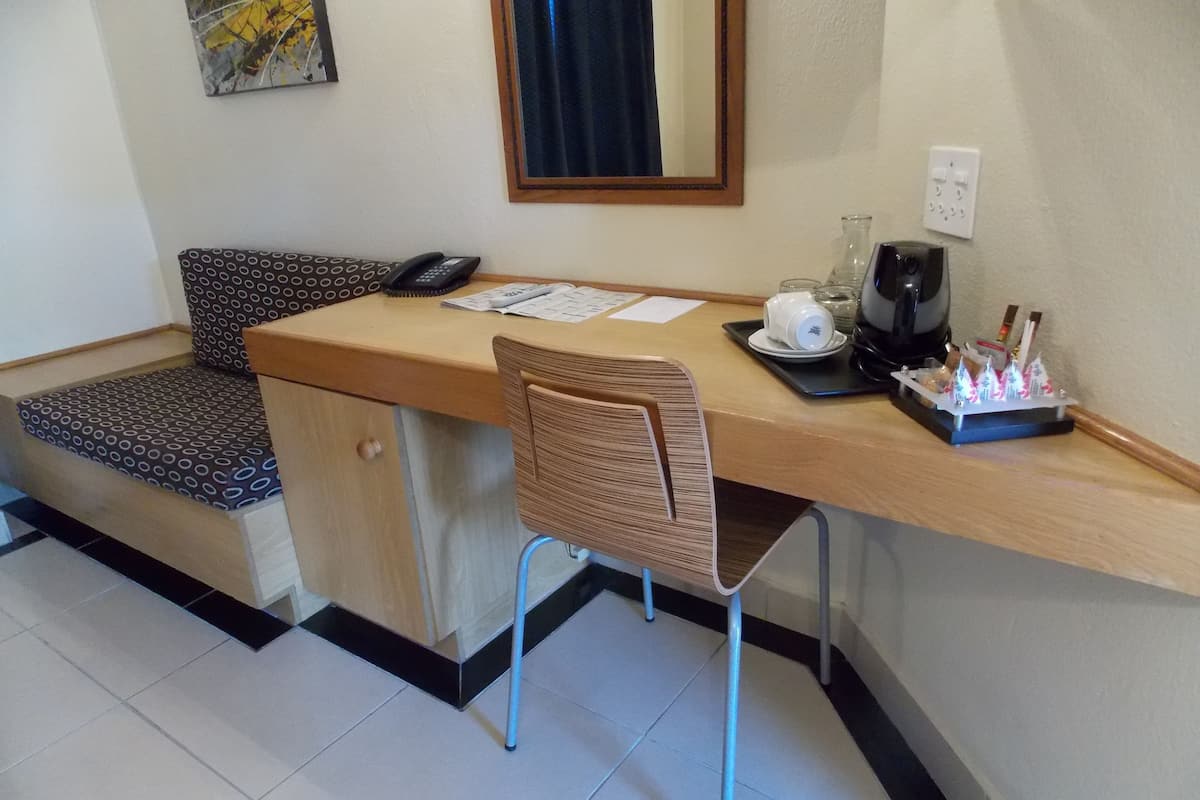 Quarto pequeno e aconchegante com uma escrivaninha de madeira, uma cadeira, um sofá, um telefone, uma cafeteira e um pequeno objeto decorativo na escrivaninha.