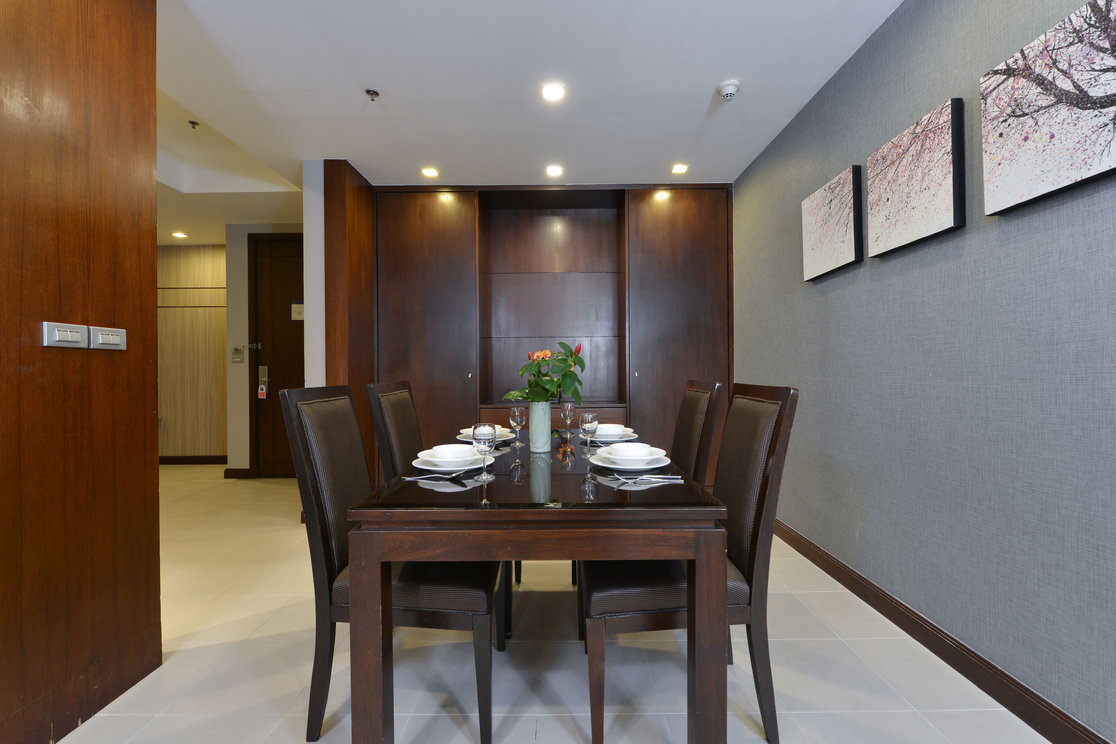 A dining area with a wooden table set for four, surrounded by chairs.