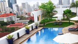 Une piscine sur le toit offrant une vue panoramique sur la ville, entourée de plantes en pot et de chaises longues.