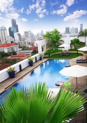Una piscina en la azotea con vistas al horizonte urbano, rodeada de macetas con plantas y sillas de descanso.
