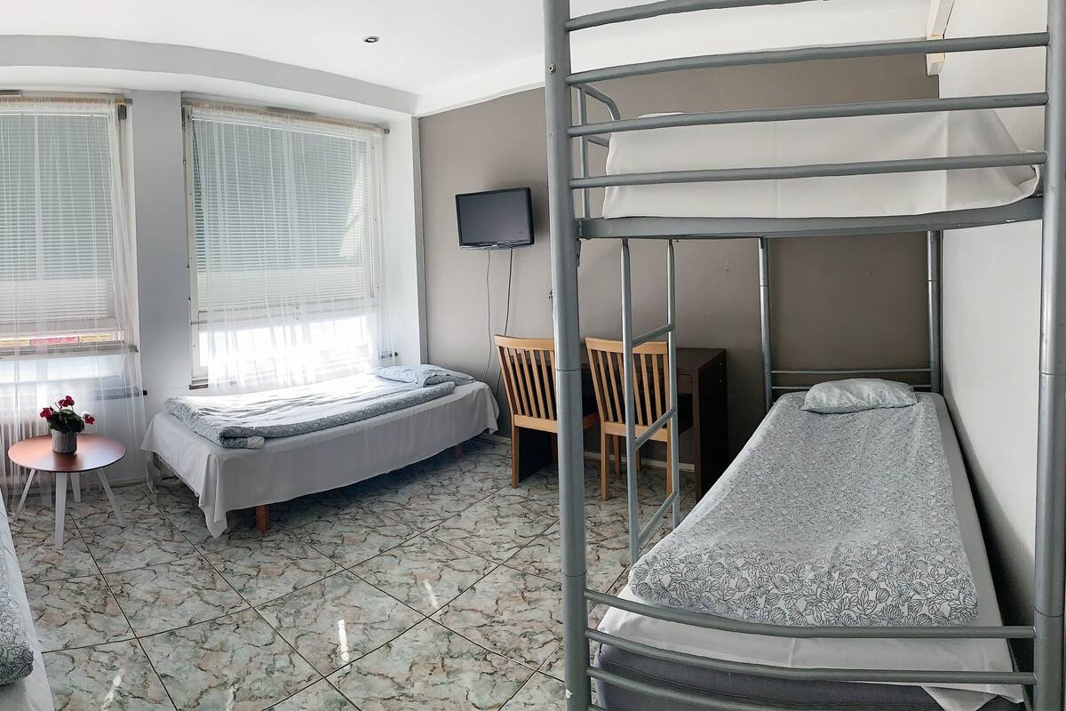 A dormitory room with bunk beds, a small table with a plant, and a TV on the wall.