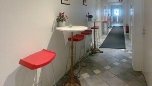 En gang med en række røde barstole, et rundt hvidt bord og plantekasser.