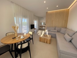 Una sala de estar moderna con una mesa de comedor de madera, un sofá gris y un televisor montado en la pared.