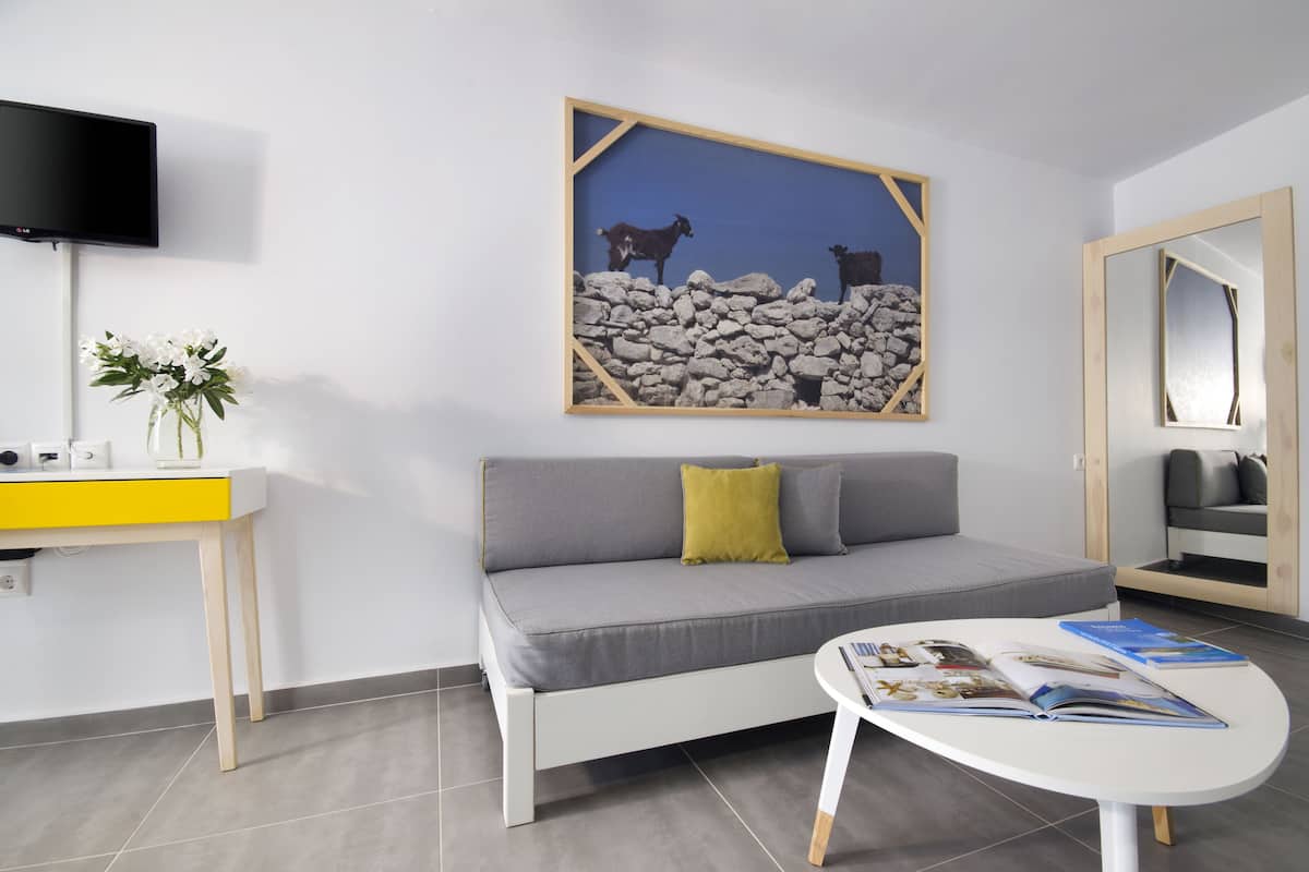 Una sala de estar moderna con un sofá gris, una mesita con revistas, un televisor montado en la pared y un cuadro con cabras en una pared de roca.