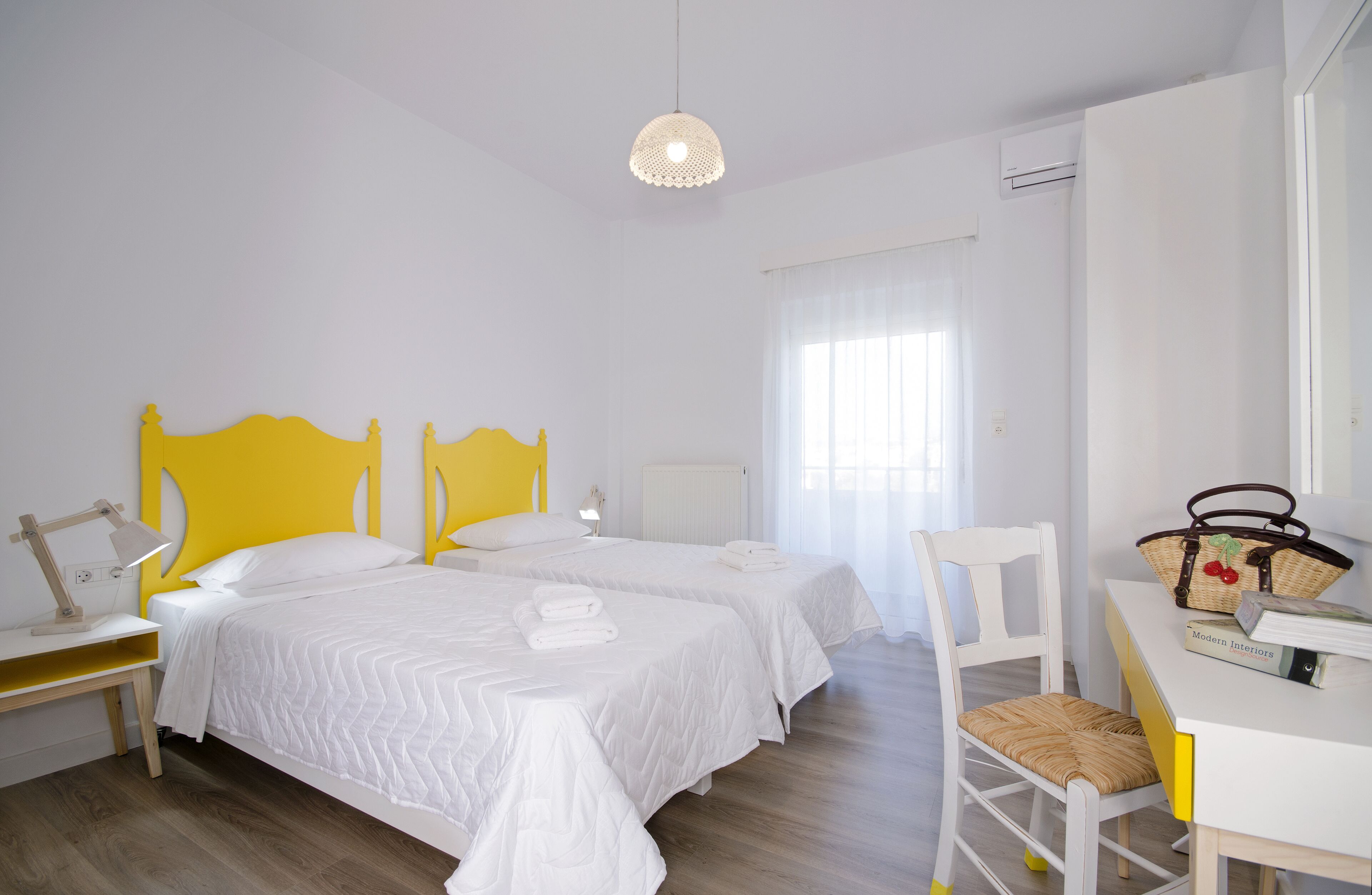 A bedroom with two beds, a desk, a chair, and a hanging light fixture.