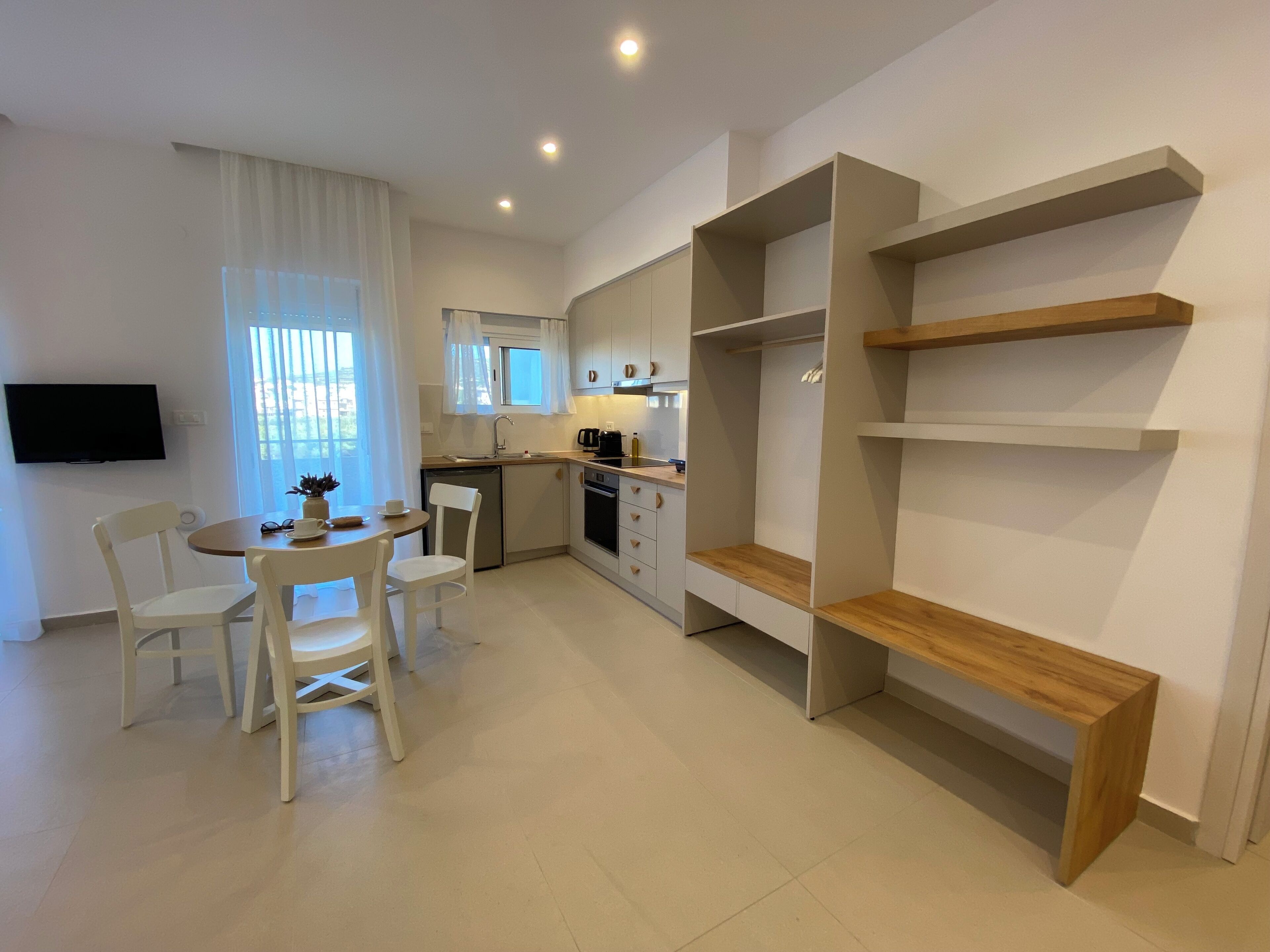Una cocina moderna con armarios blancos, un comedor con mesa y sillas, y estanterías empotradas de madera.