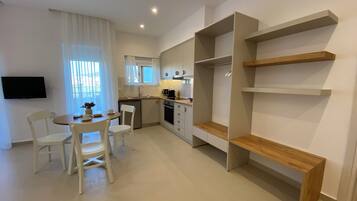Una cocina moderna con armarios blancos, un comedor con mesa y sillas, y estanterías empotradas de madera.