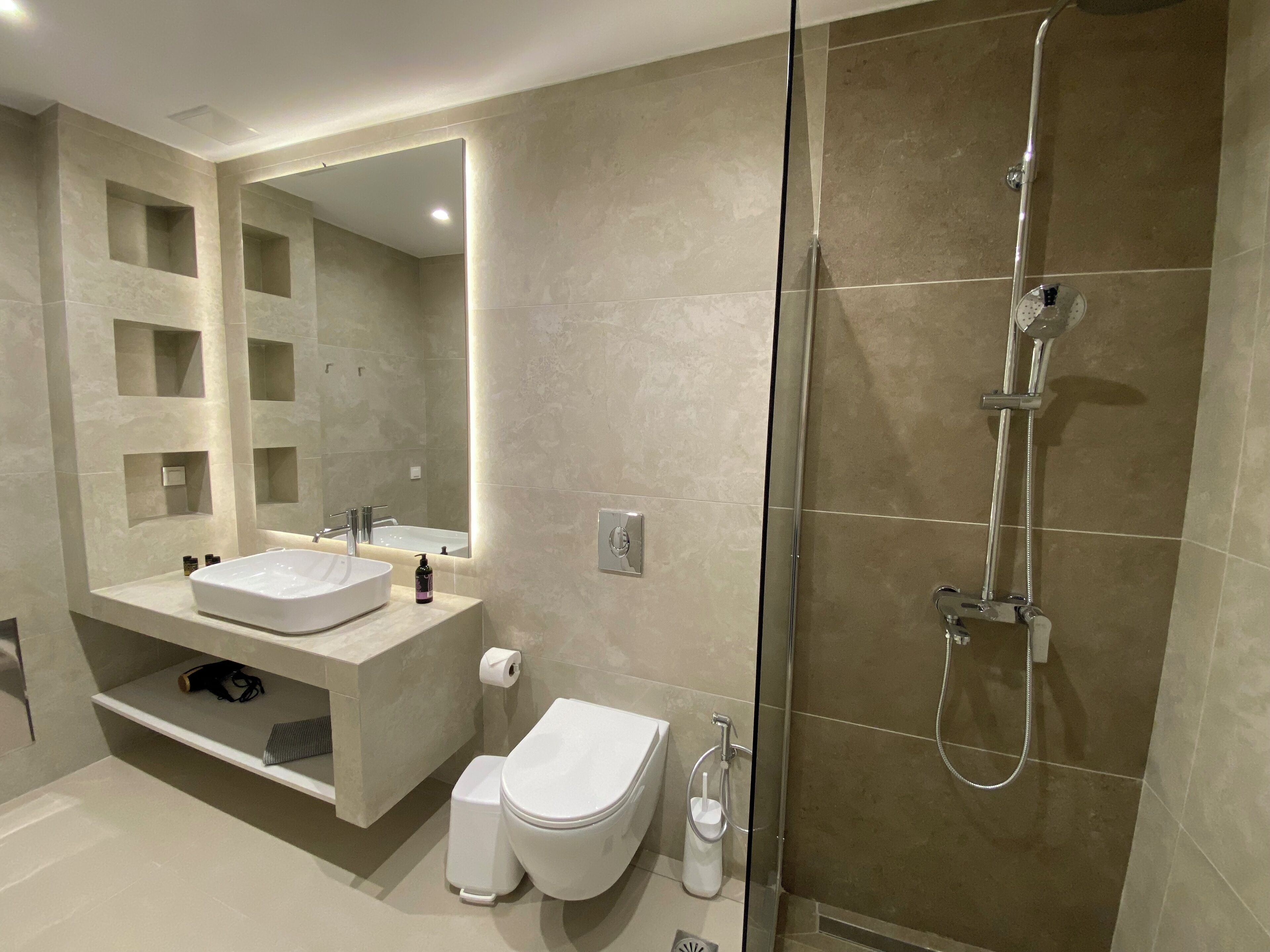 A modern bathroom with a large mirror, a sink, a toilet, and a shower.