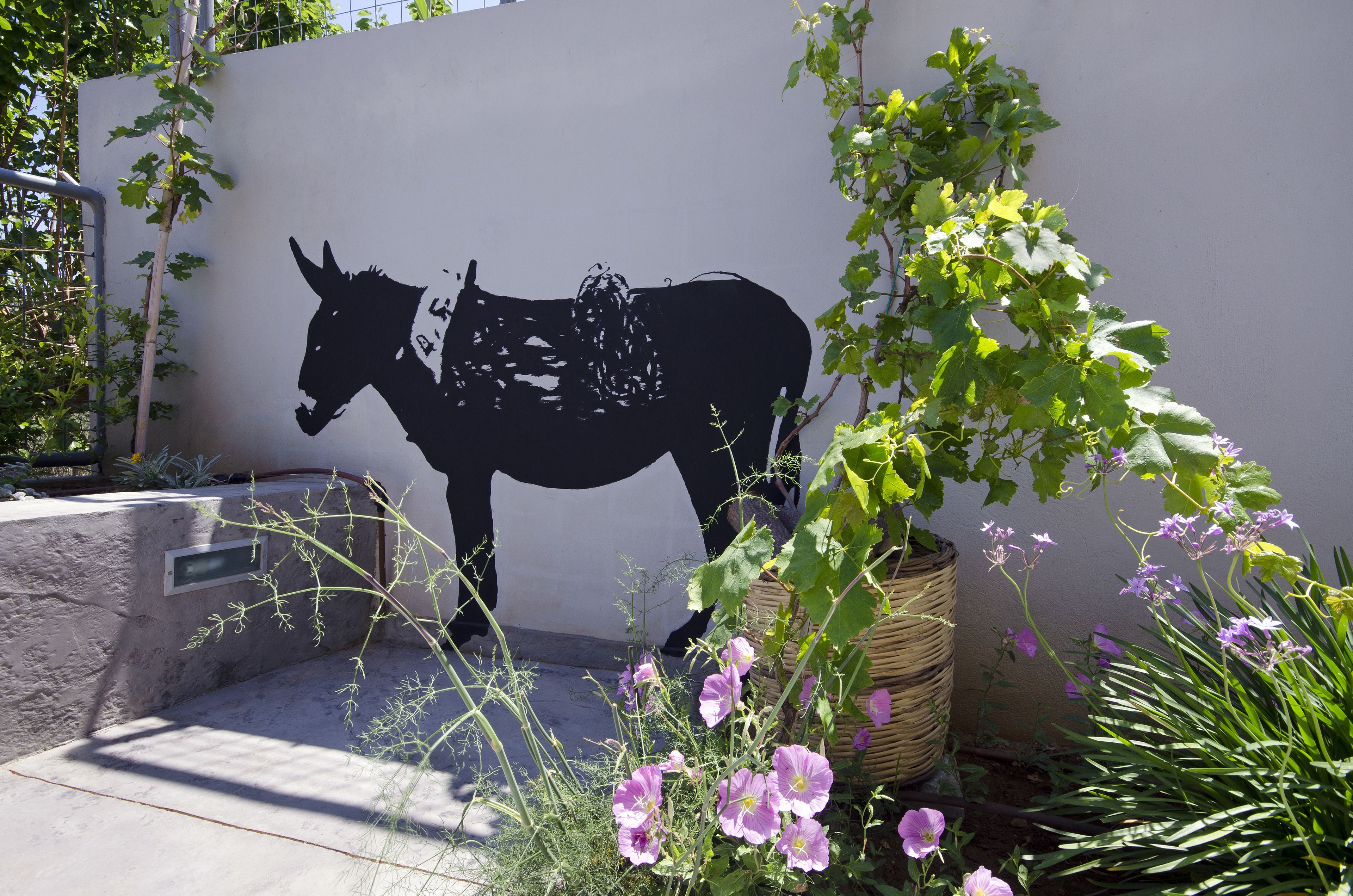Silueta negra de un burro montada en la pared, rodeada de follaje y flores.