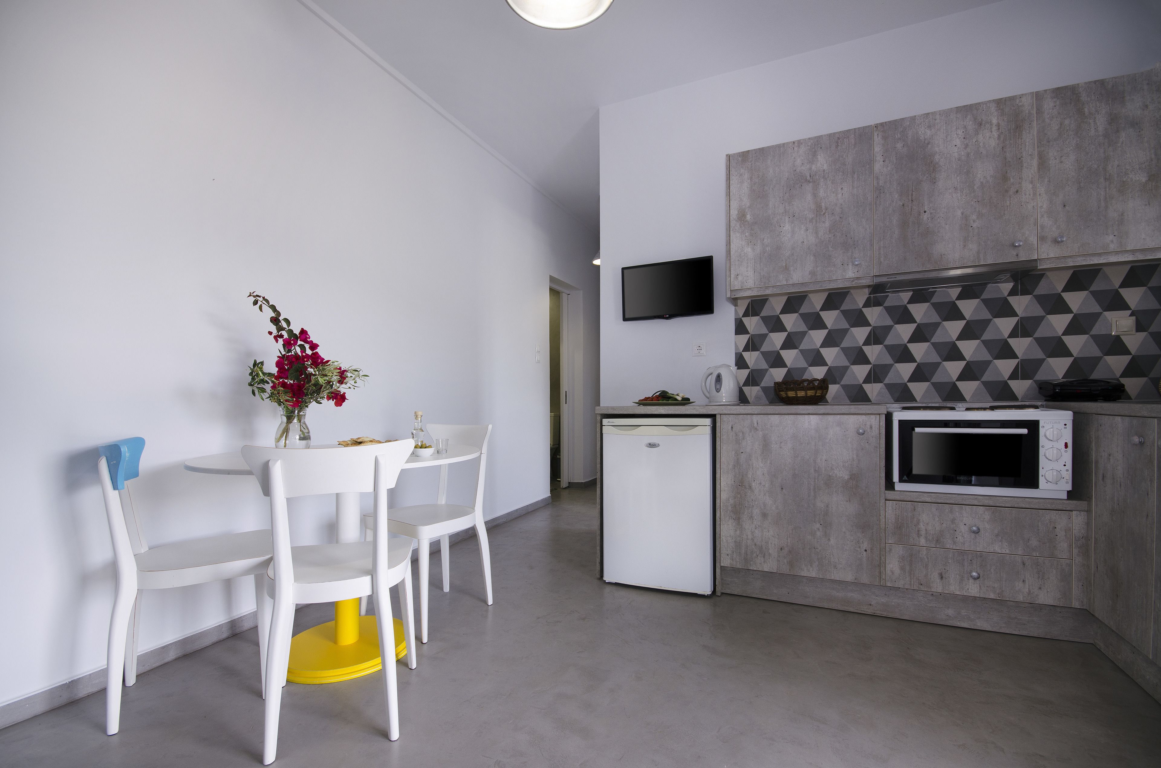 A modern kitchen with a built-in microwave, a small refrigerator, and a dining area with white chairs and a table.
