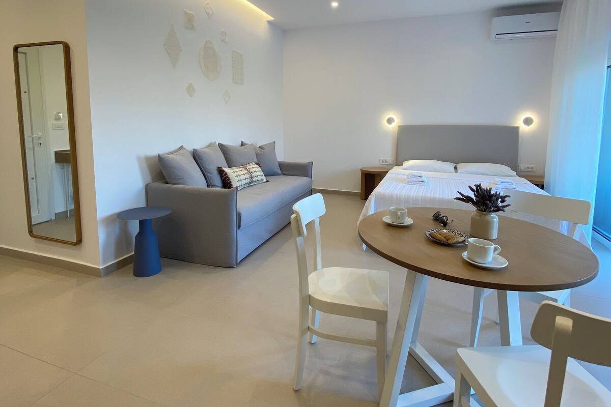 Una habitación de hotel moderna con cama, sofá, mesa de comedor con sillas y una mesita auxiliar.