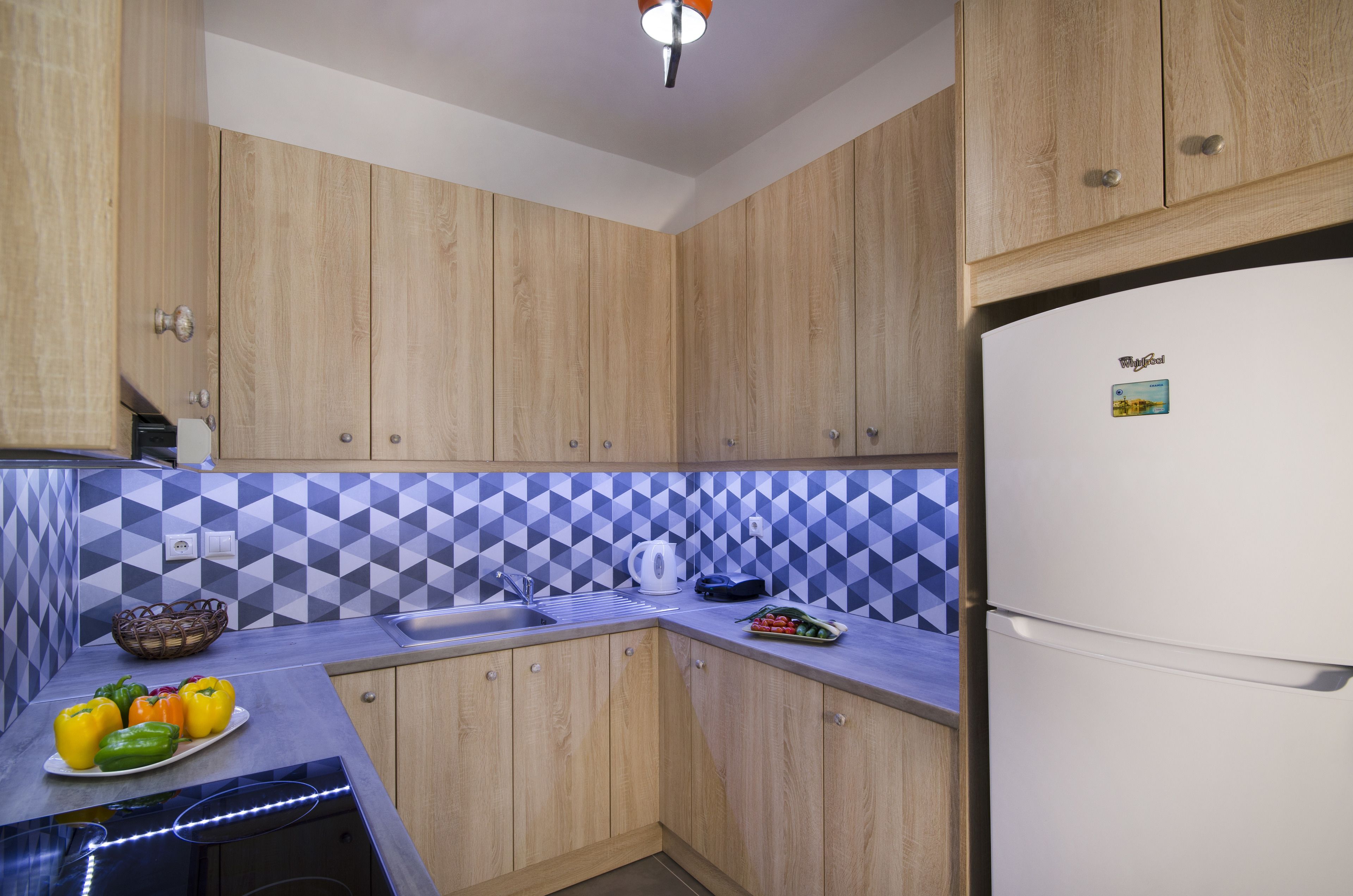 A kitchen with wooden cabinets, a white refrigerator, a sink, and a blue and white tiled backsplash.