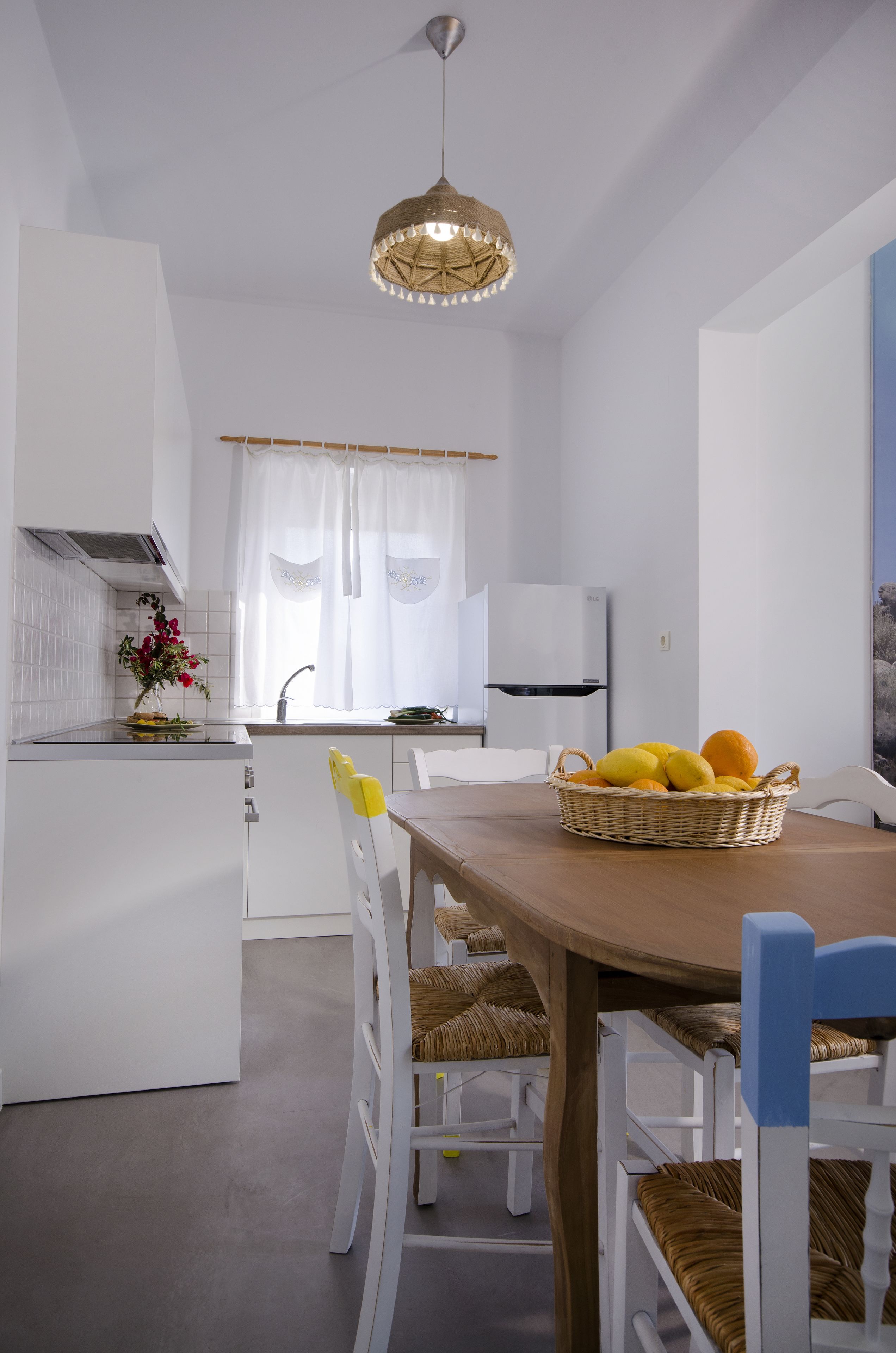 A modern kitchen with white cabinetry, a dining table with wicker chairs, and a basket of fruit on the table.