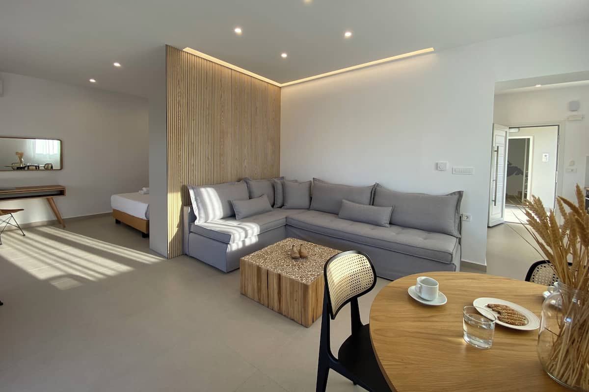 Una sala moderna con un sofá seccional, una mesa de centro redonda de madera y una mesa de comedor con una taza y galletas.