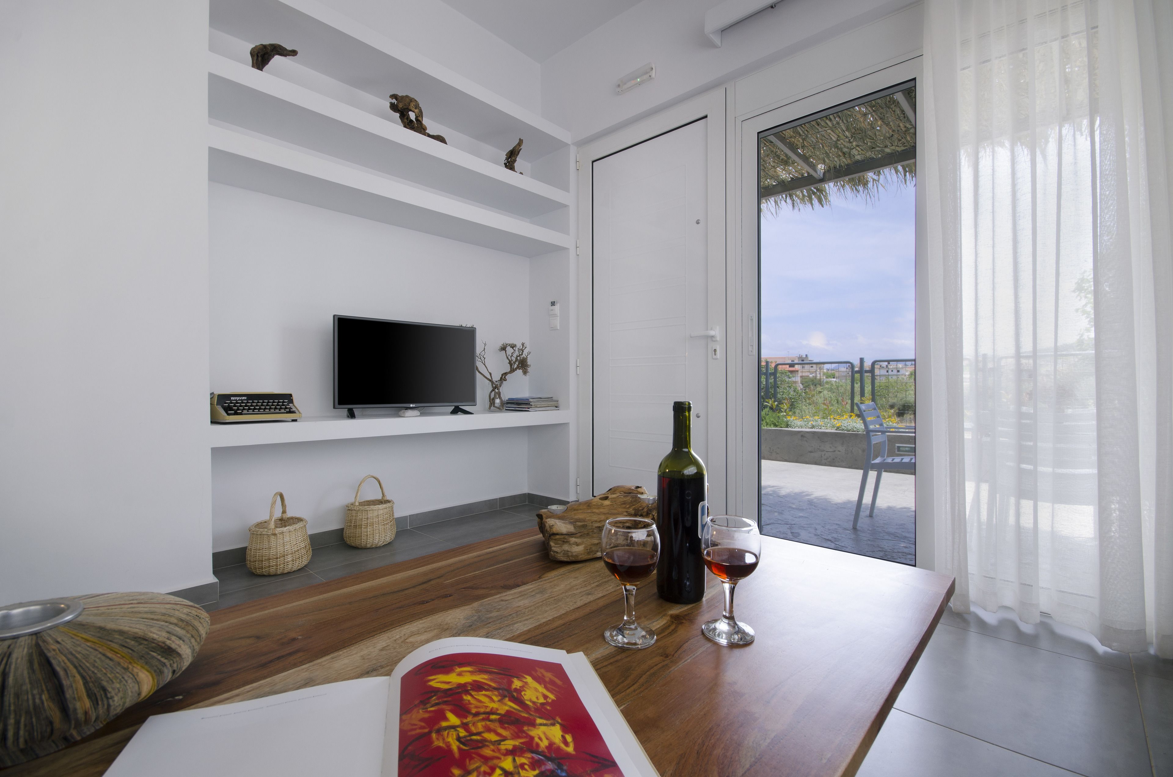 A modern living room with a flat-screen TV, wine glasses, a bottle of wine, and a wooden table.