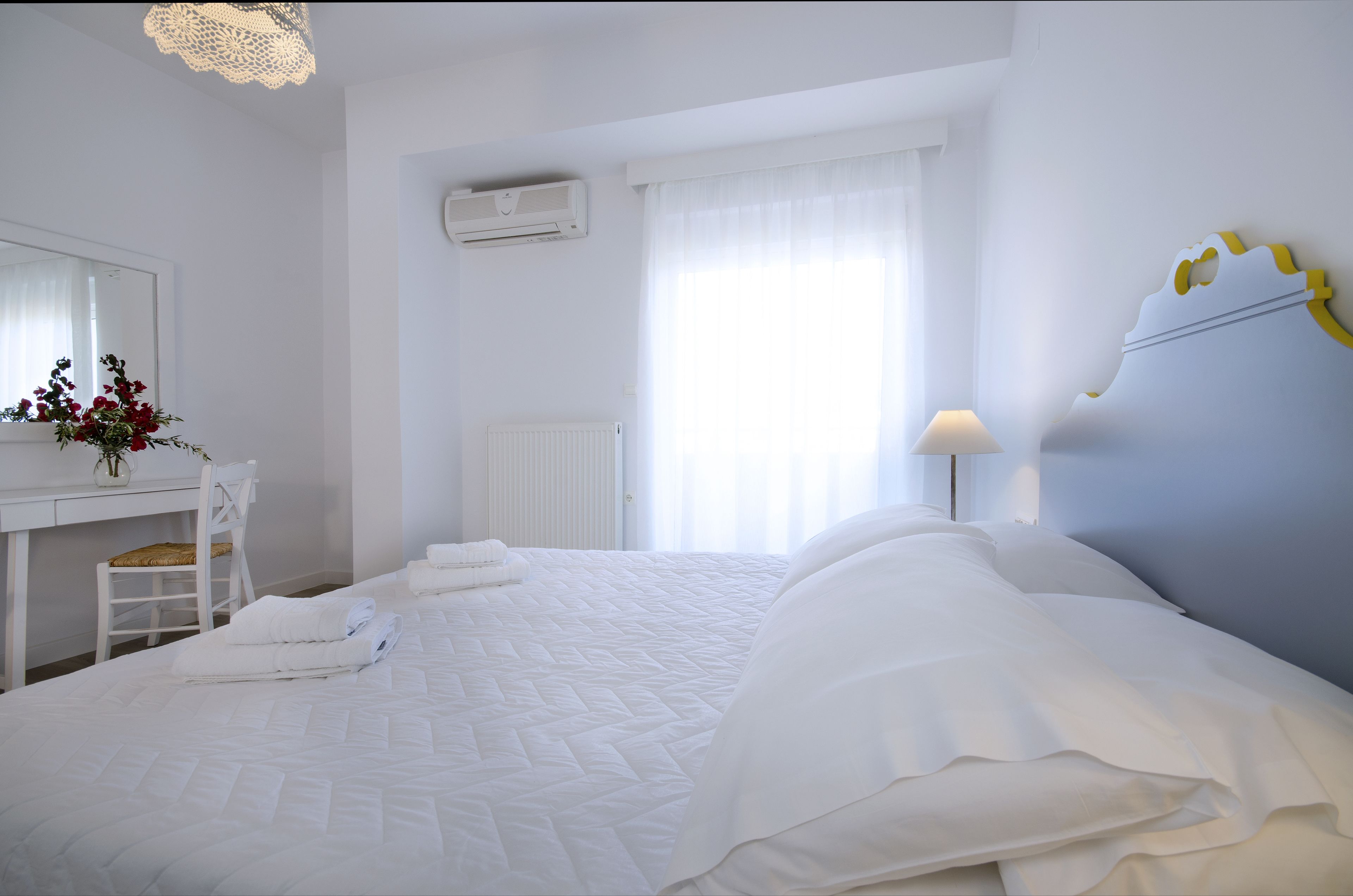Une chambre d’hôtel avec un lit bien fait, un bureau avec une chaise, un radiateur et une fenêtre avec des rideaux.