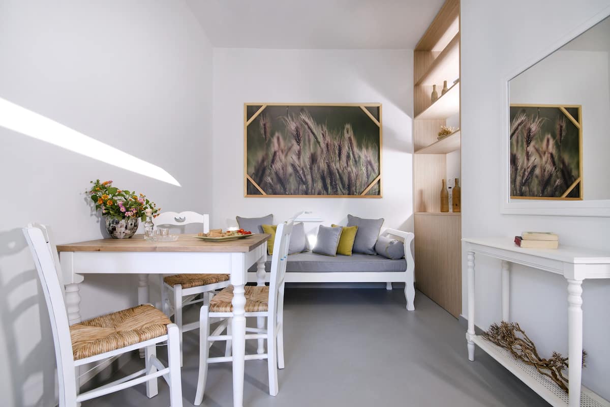 Un comedor con una mesa blanca, sillas y un sofá. Hay pinturas en las paredes y una estantería con botellas.