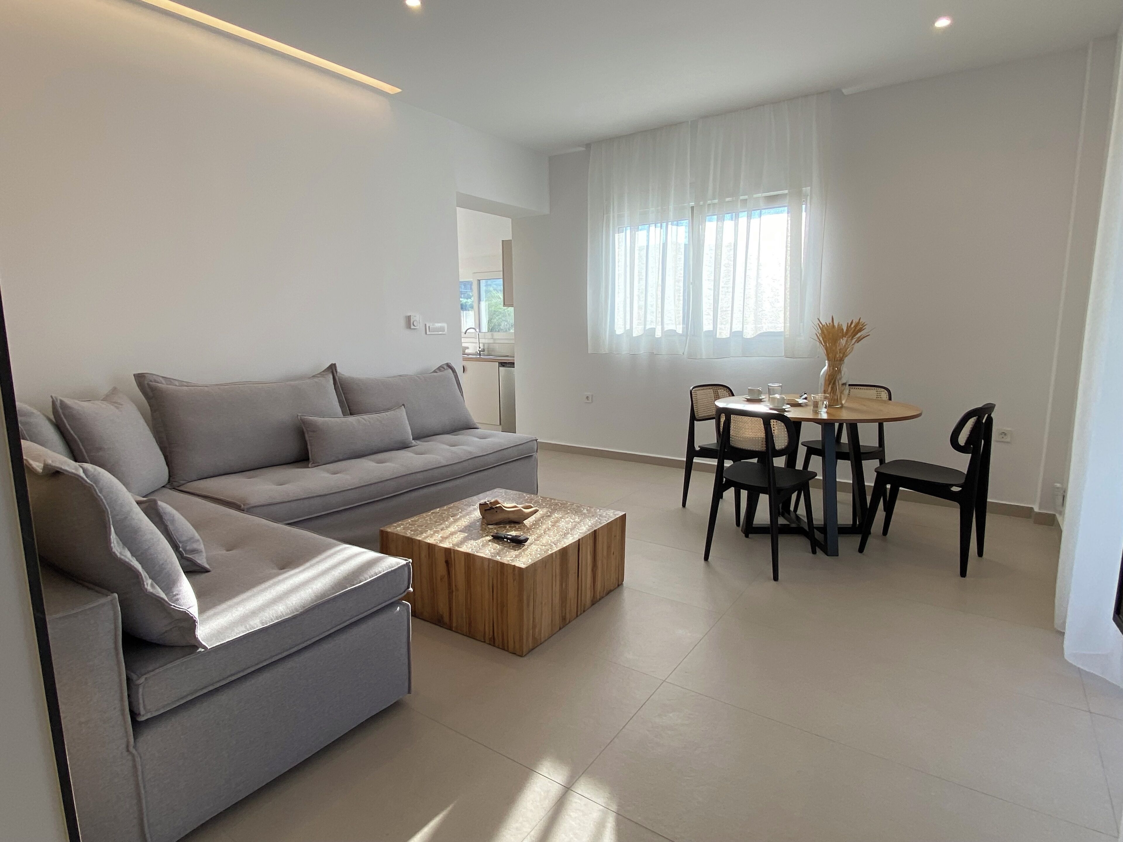 A modern living room with a grey sofa, a wooden coffee table, and a dining area with a table and chairs.